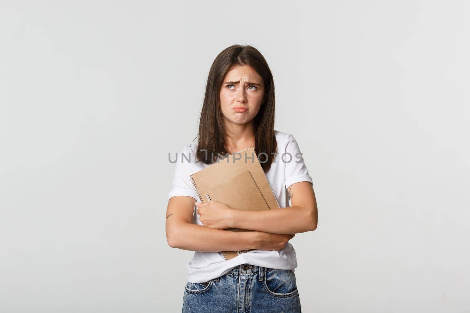 Portrait of sad and disappointed cute female student holding notebooks and looking upper left corner upset by Benzoix