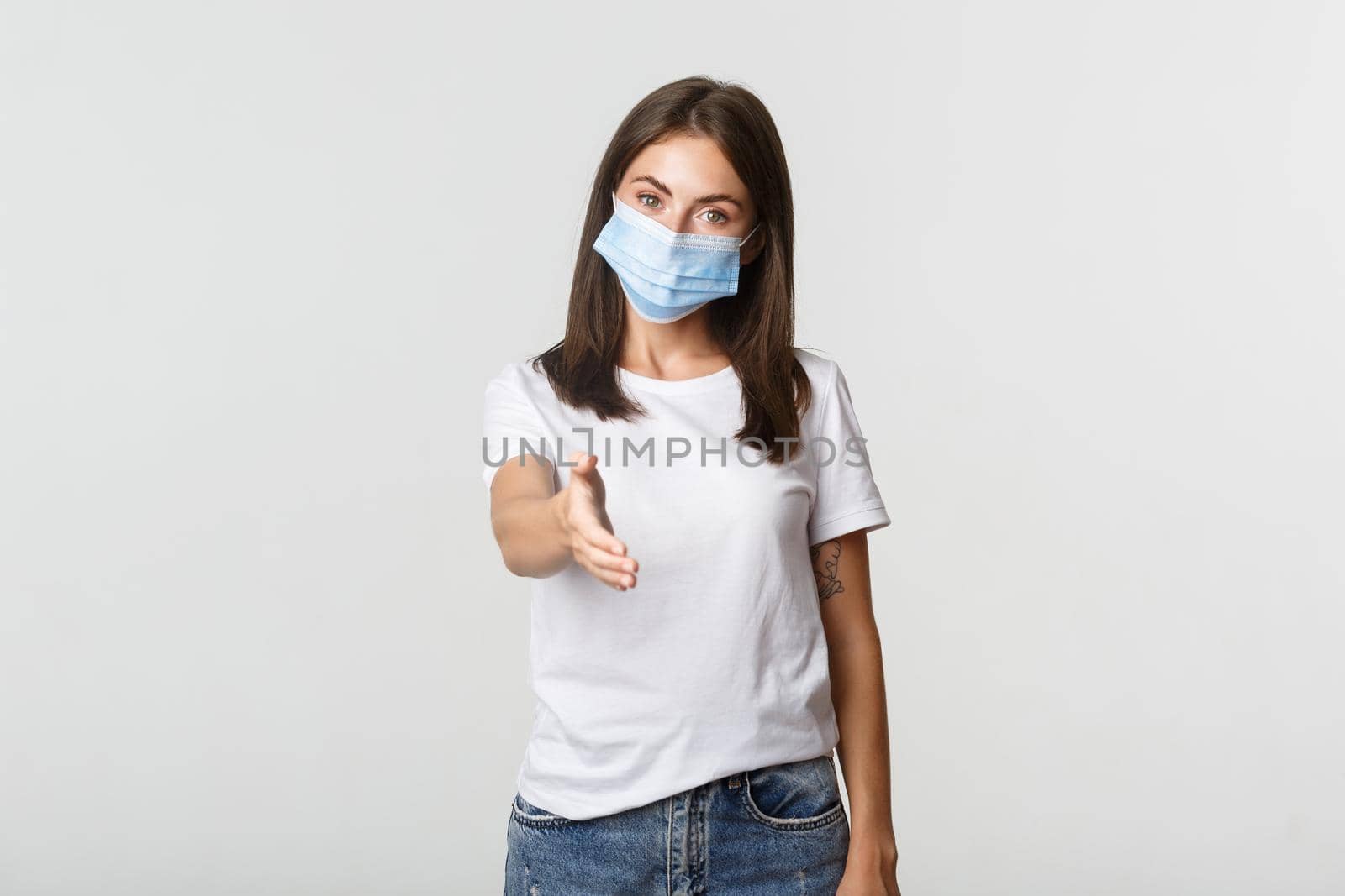 Covid-19, health and social distancing concept. Portrait of friendly attractive young woman in medical mask, extending hand for handshake by Benzoix
