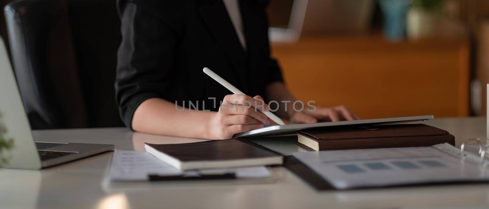 Close up hand of woman with stylus pen writing on digital tablet, touching on digital tablet screen working on laptop computer in office.