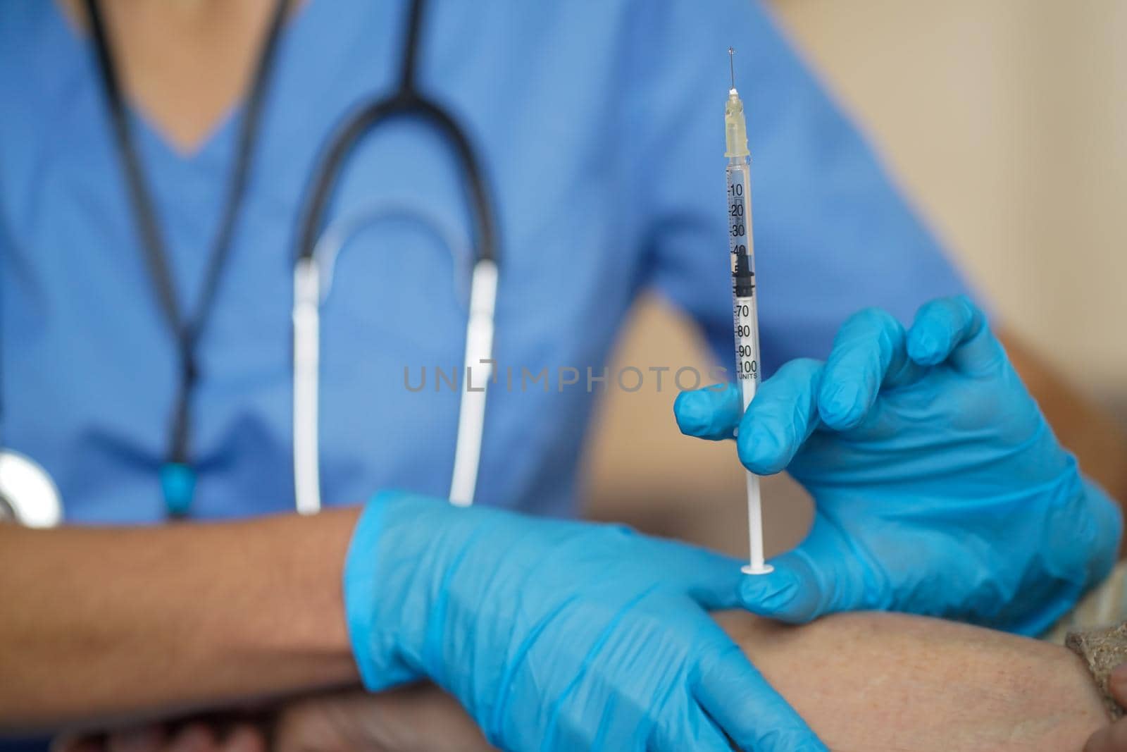 The nurse makes an injection with the vaccine to the patient at home. A young doctor in a blue suit holds the hand of woman and is about to give an injection with a syringe. Medicine and healthcare.