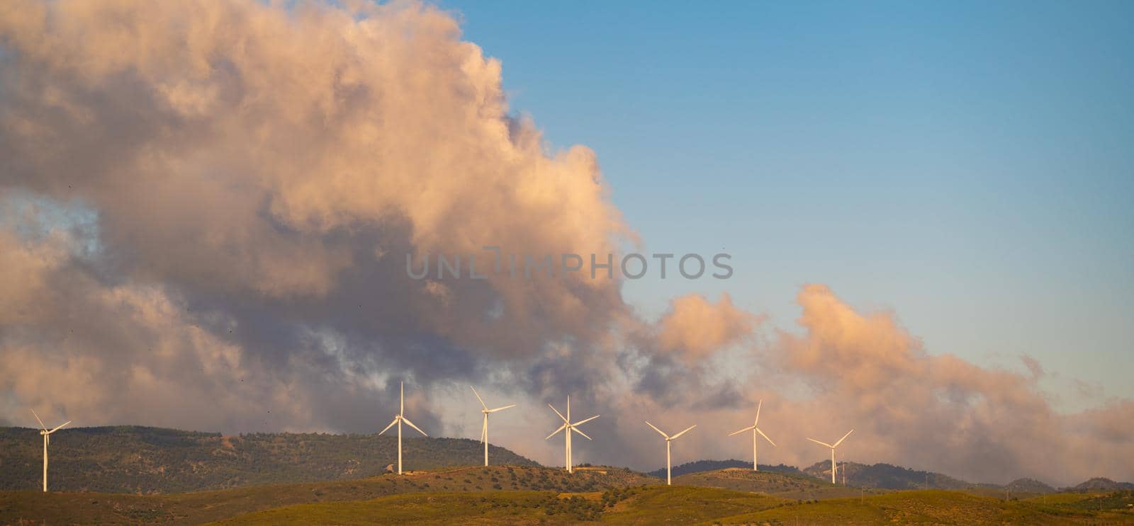 meadows with windmills and dramatic sunset with warm clouds