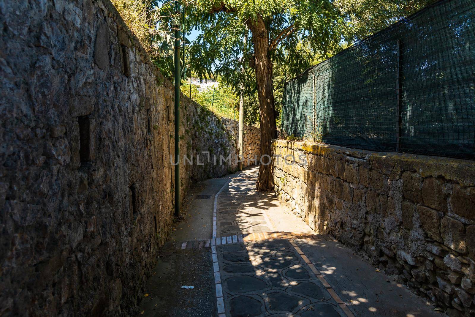 Very narrow street with high stony fences and a lot of shadows by Wierzchu