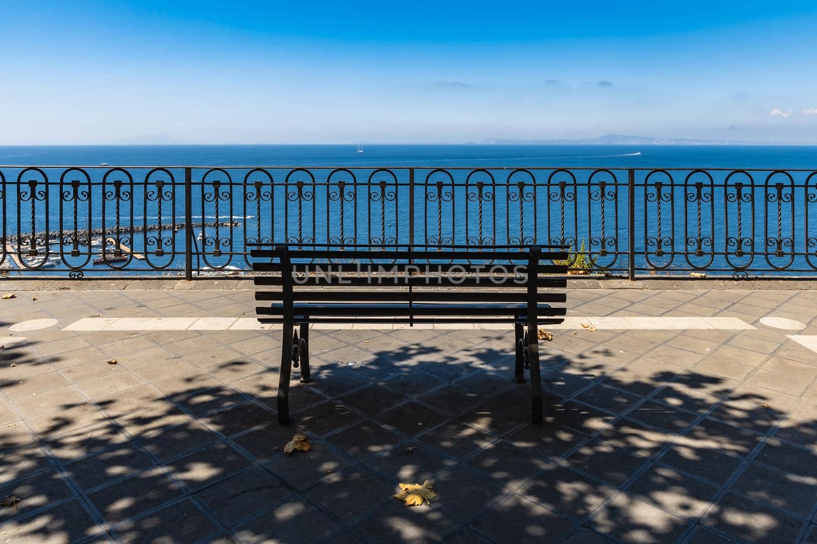 Small bench standing on the edge in front of metal railing with beautiful view to the sea by Wierzchu