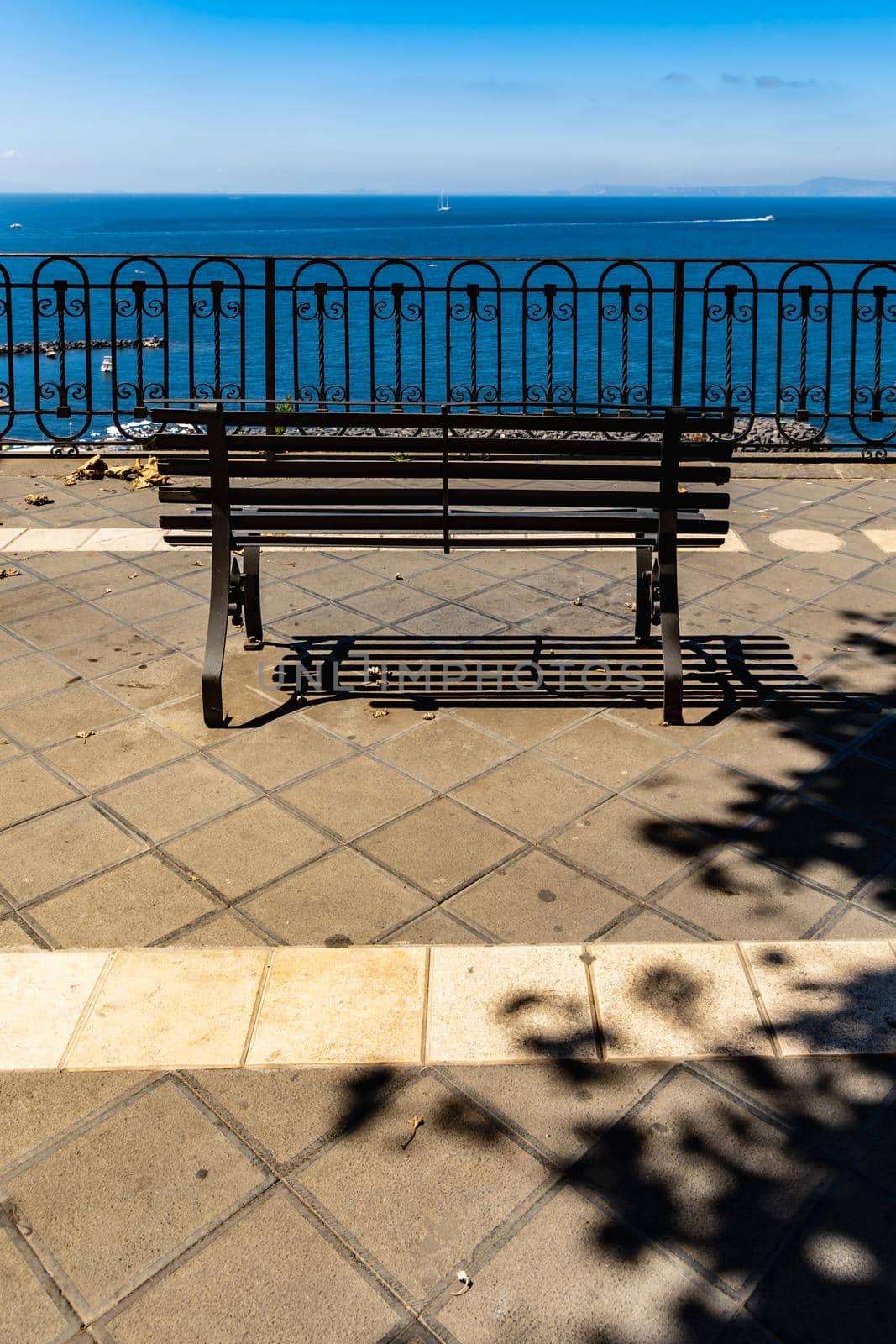 Small bench standing on the edge in front of metal railing with beautiful view to the sea by Wierzchu