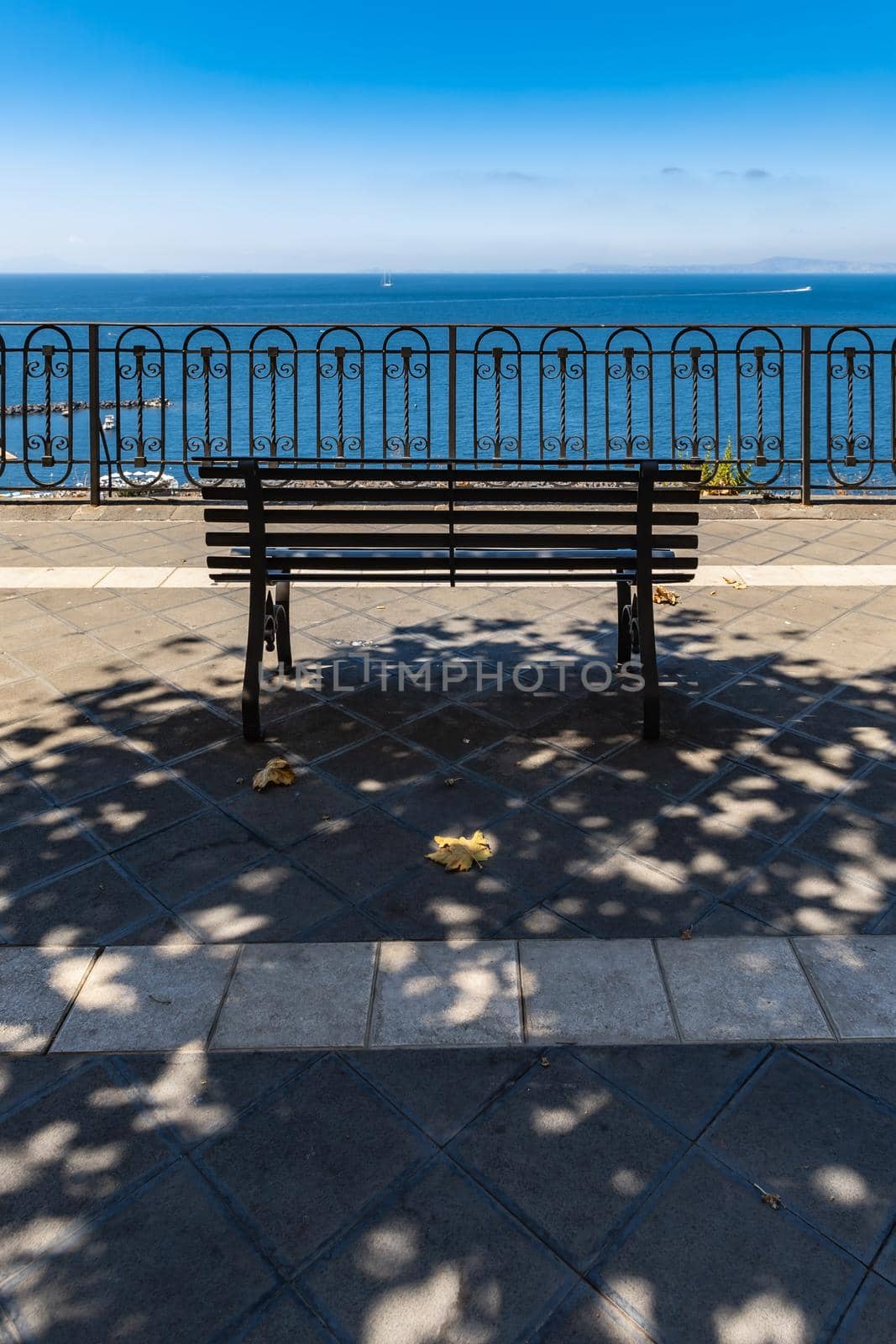 Small bench standing on the edge in front of metal railing with beautiful view to the sea by Wierzchu