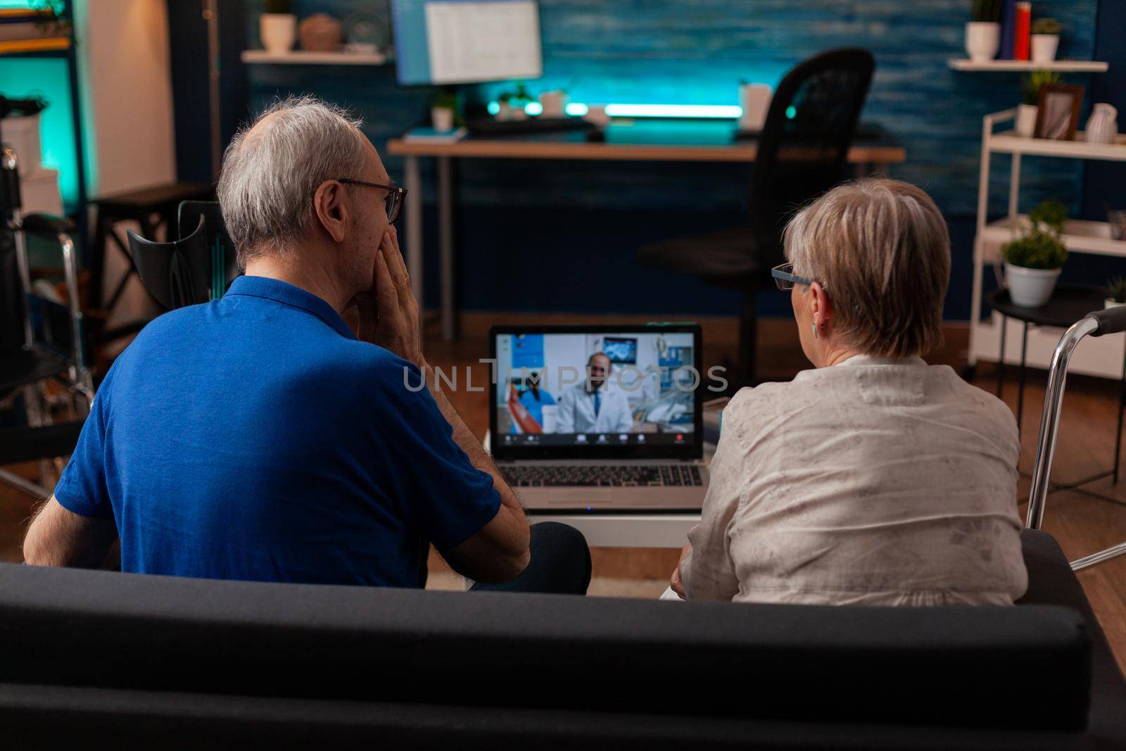 Elder people using video call conference on laptop with dentist while sitting on living room couch. Senior man with tooth ache doing dental appointment on online remote communication.