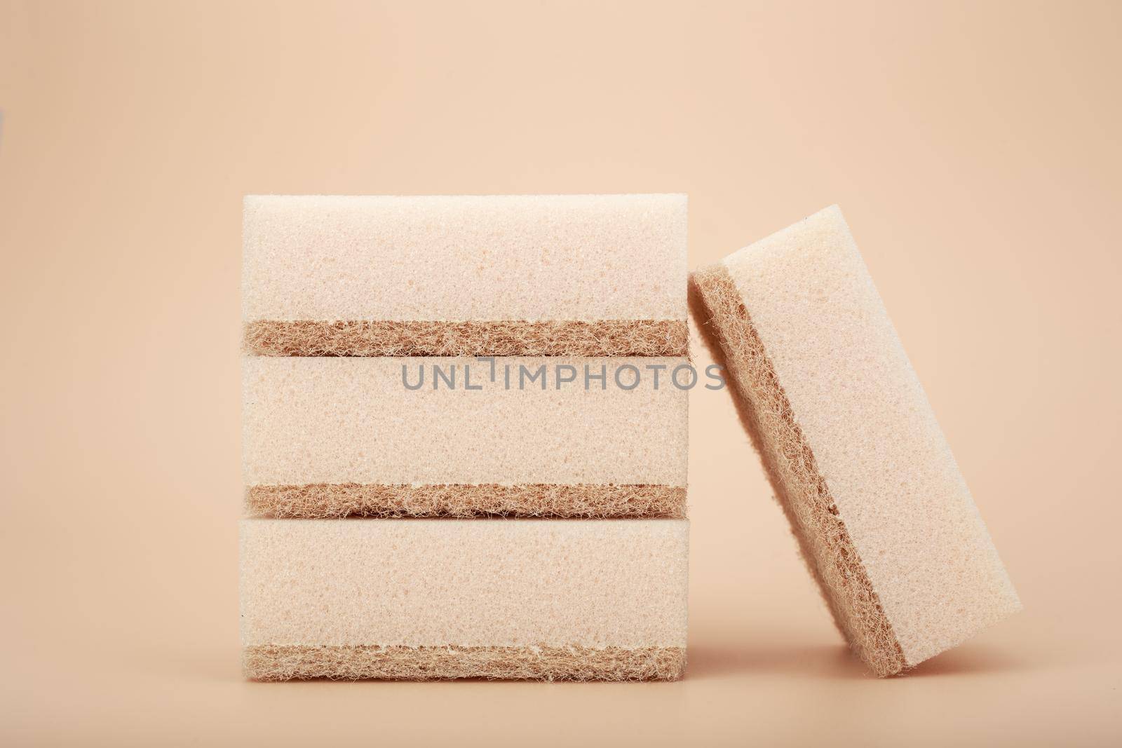 Close up of stack of four beige cleaning or kitchen sponges on bright beige background by Senorina_Irina