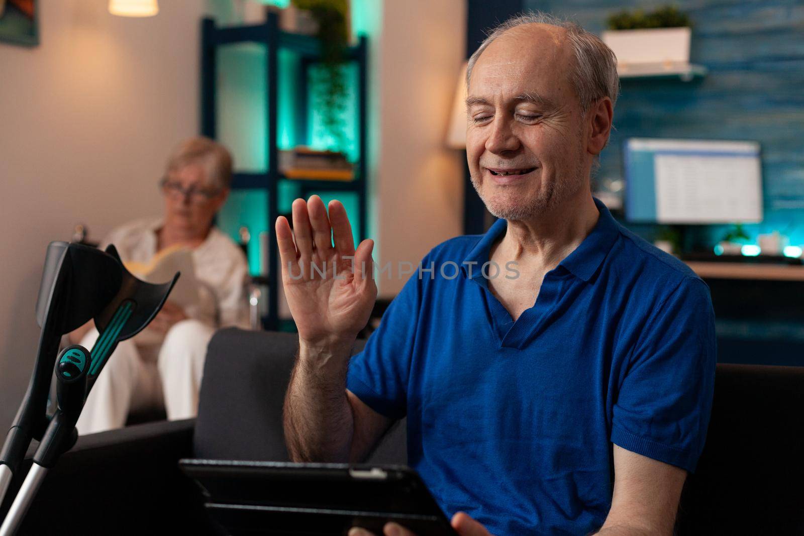 Retired adult waving at tablet with video call conference by DCStudio