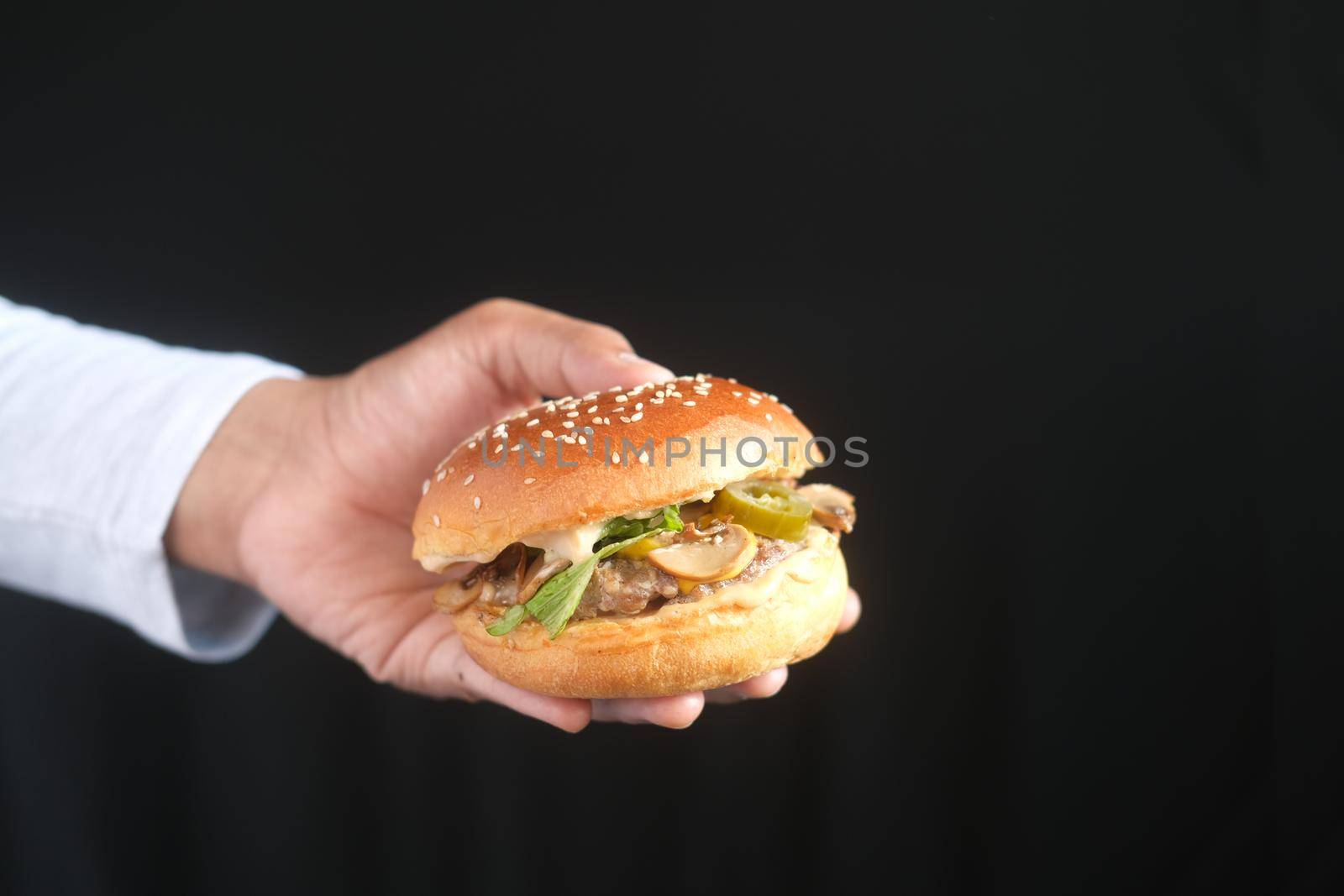 hand holding beef burger isolated on black .