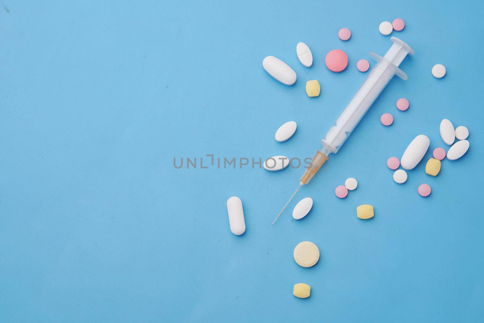 syringe and pills on blue background, close up .