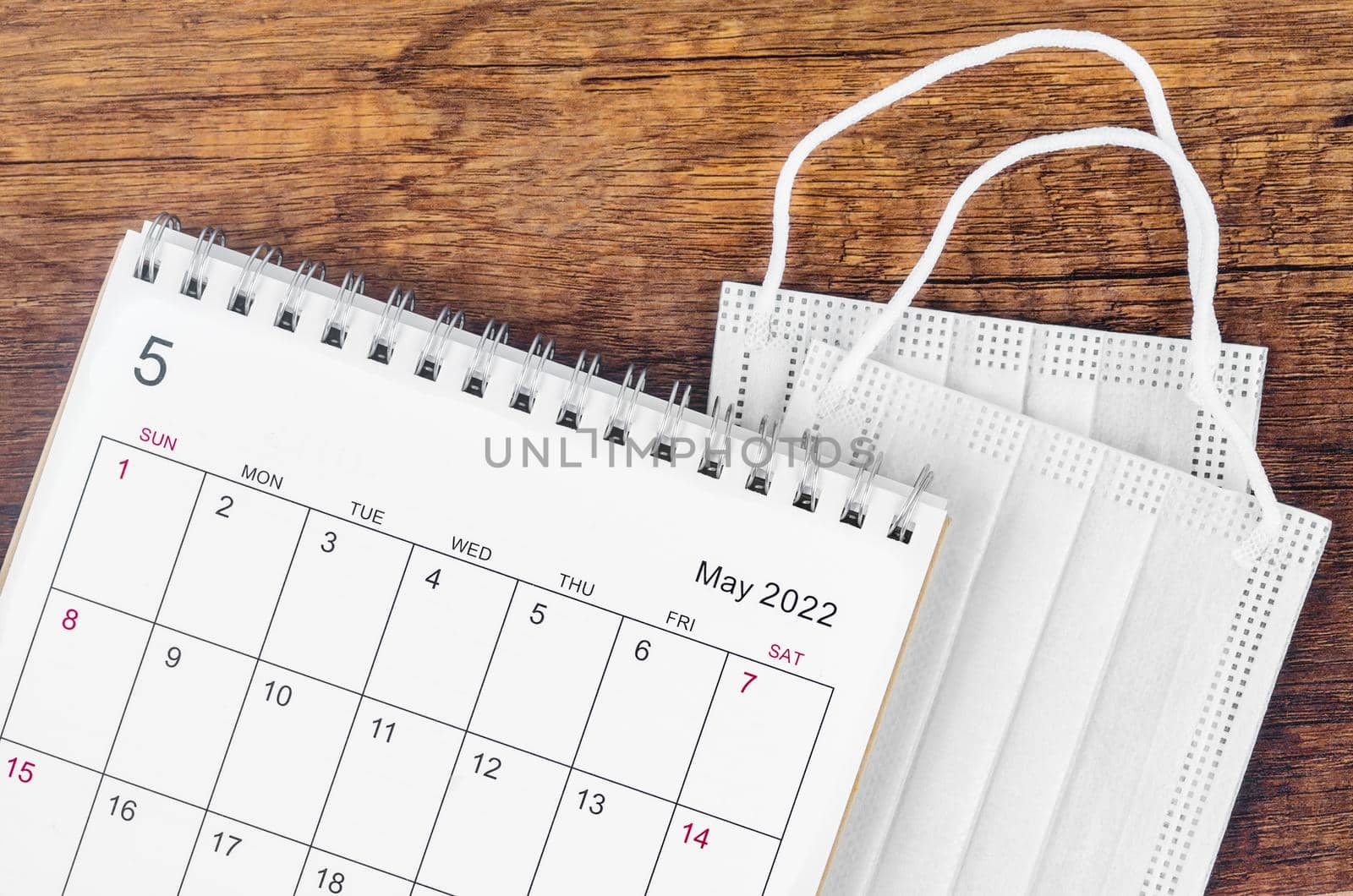 The May 2022 desk calendar with surgical mask medical on wooden background.