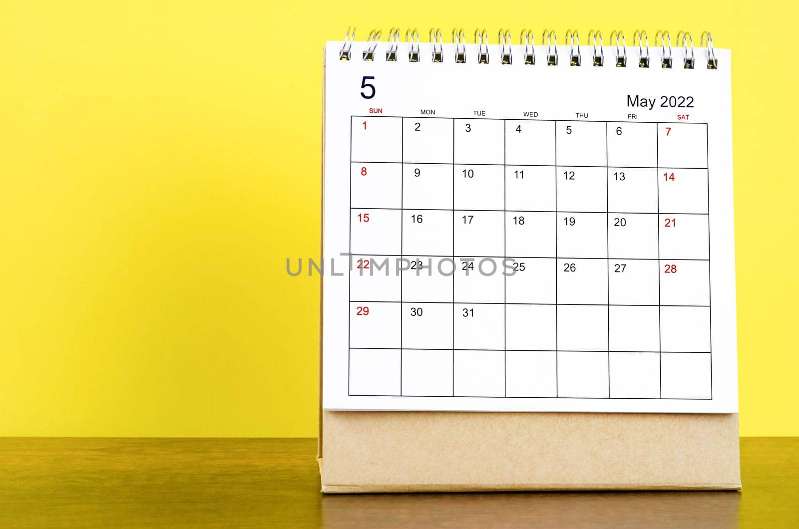 The May 2022 desk calendar with yellow background on the wooden table.