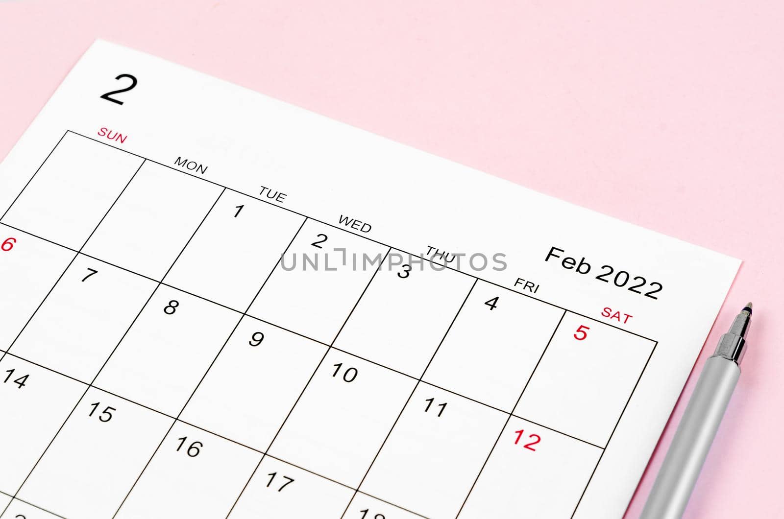 Close up February 2022 calendar sheet with pen on pink background.