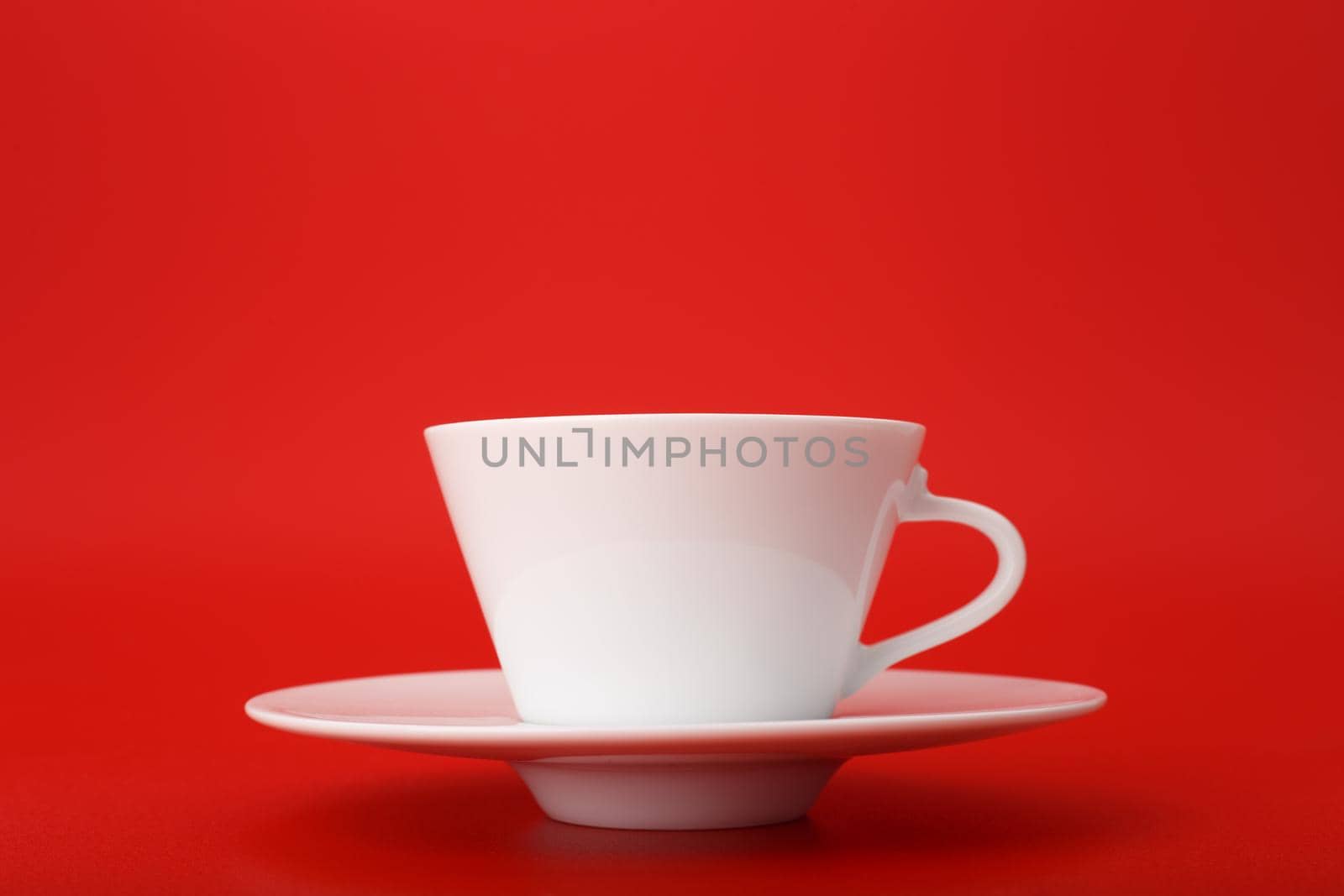 Close up of white ceramic coffee or tea cup with saucer isolated on bright red background with copy space by Senorina_Irina