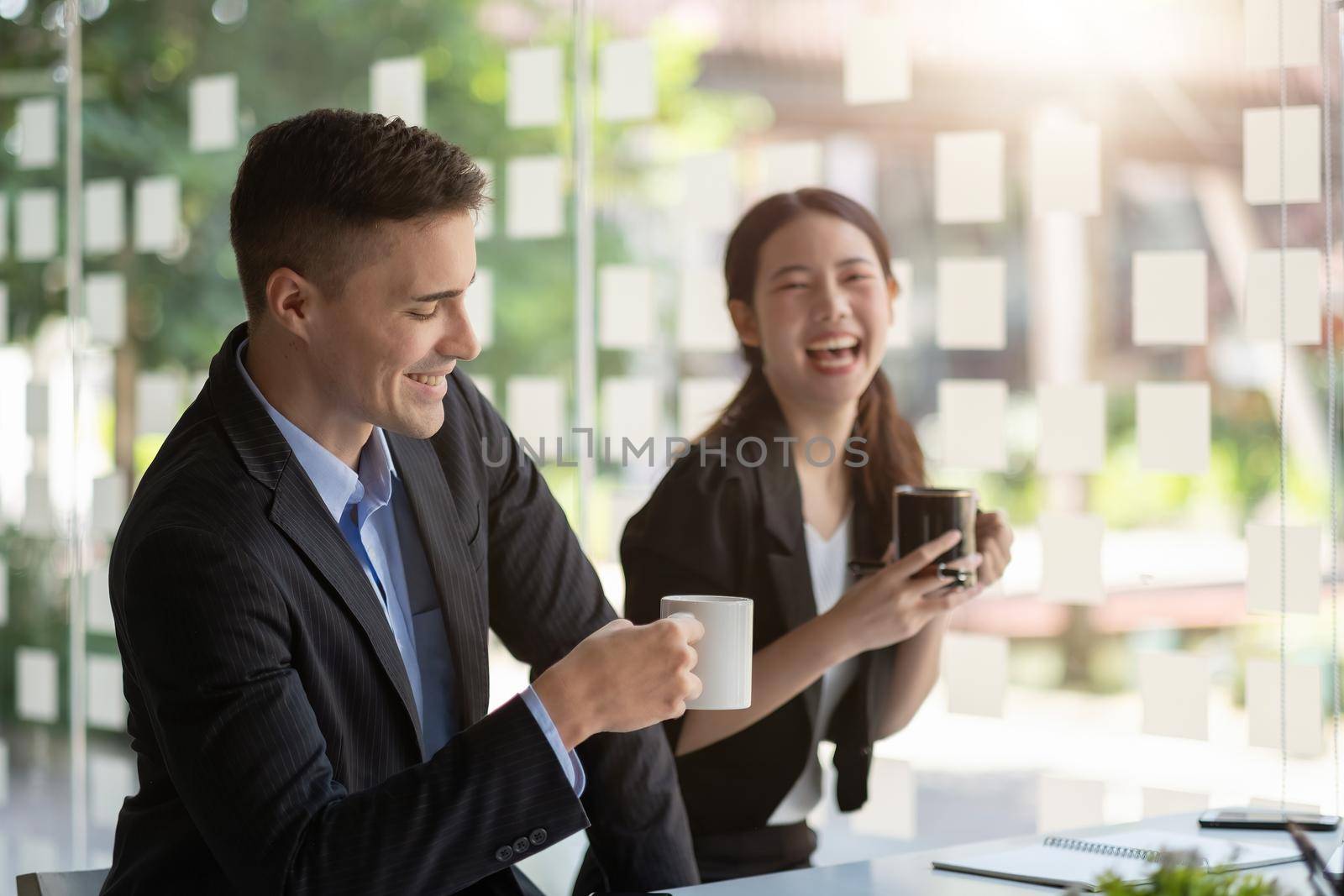 Friendly male leader laughing at group business meeting, happy young businesswoman enjoying fun conversation with partner, smiling business coach executive talking to colleague.