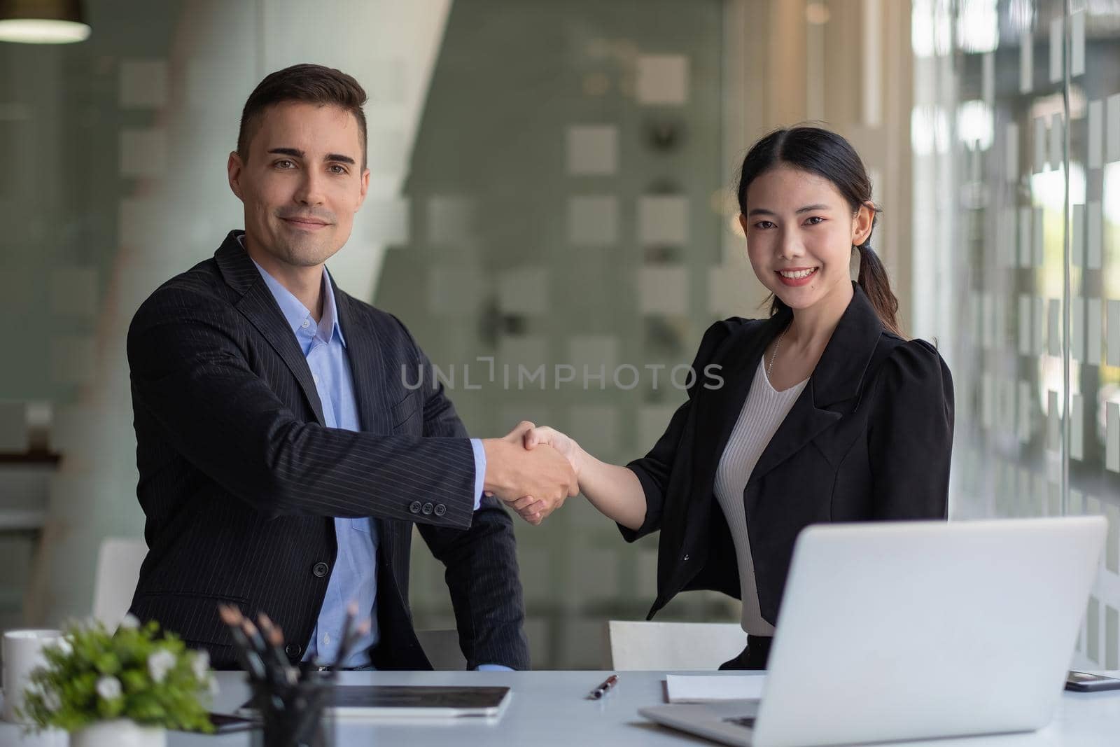 Happy caucasia male and asian female hand shaking, successful businessman handshake after good deal for both companies, business merger and acquisition concept by nateemee