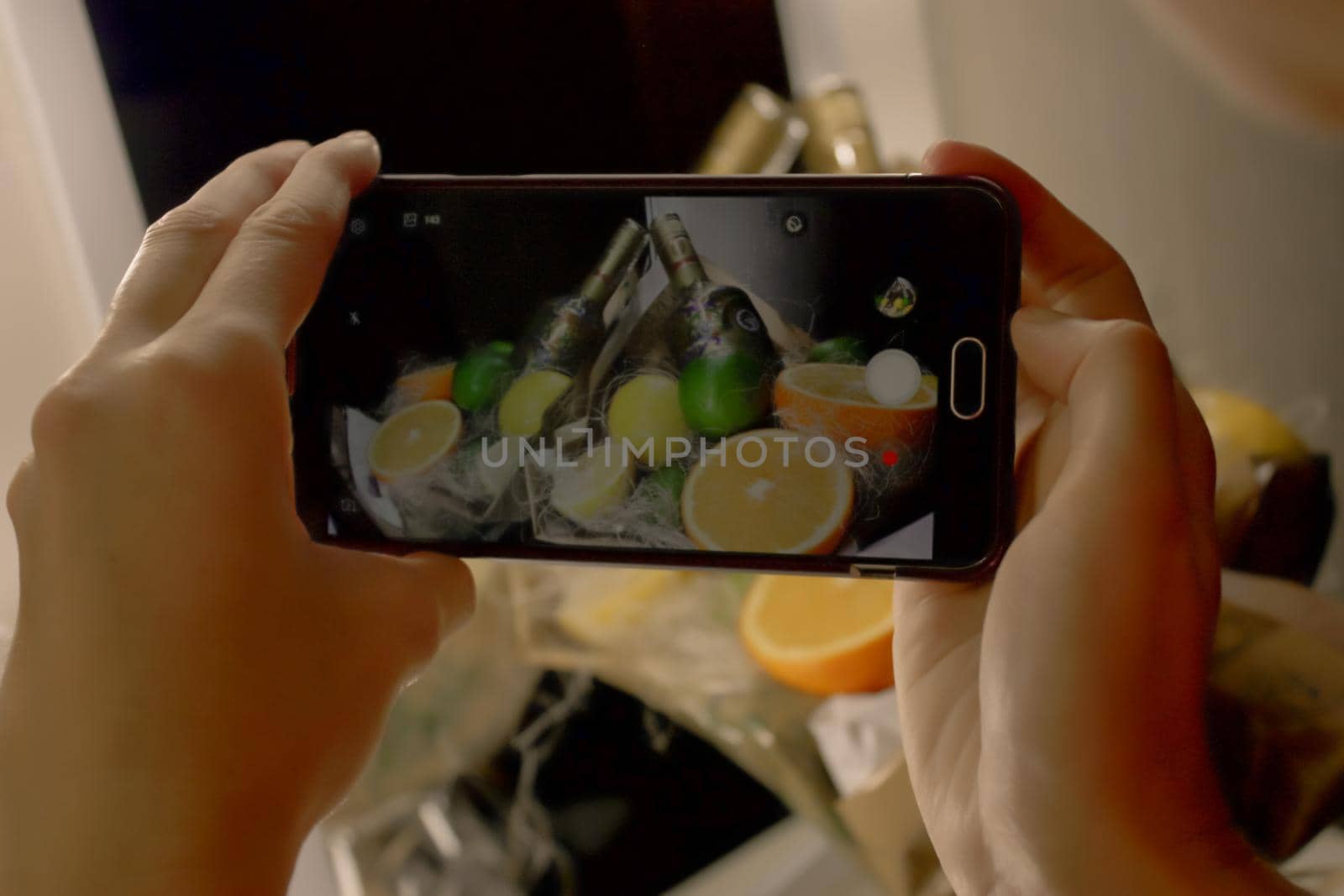 wo hands hold a smart phone and takes a composition of oranges and bottles of champagne