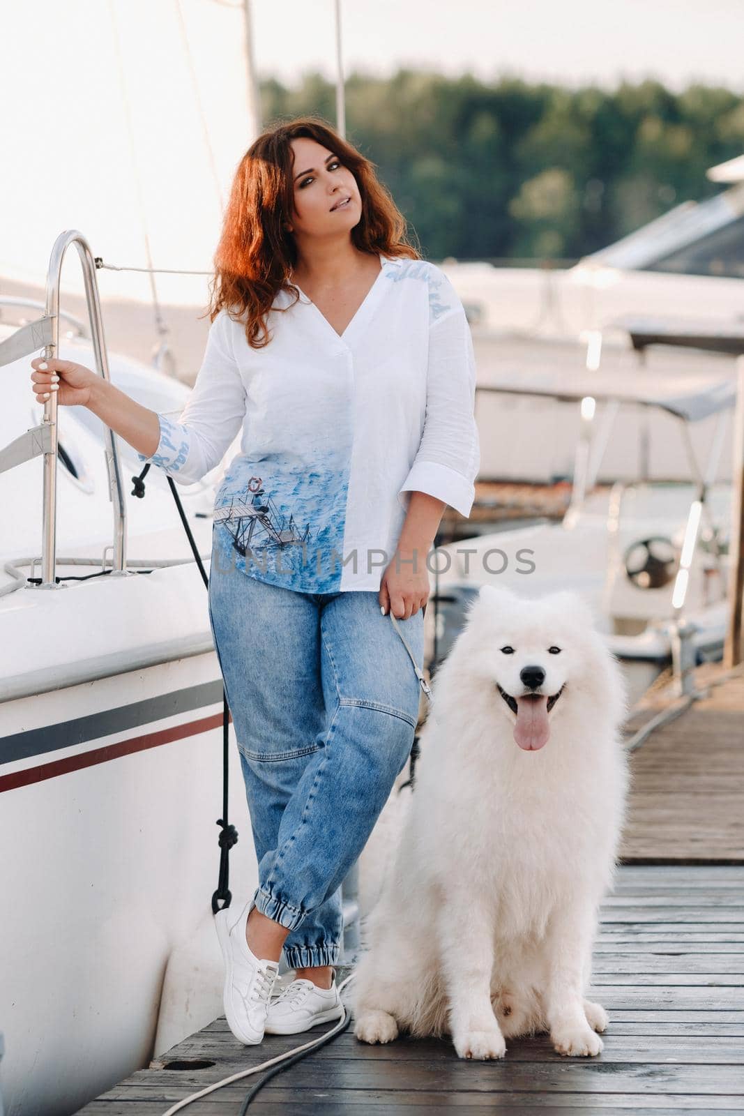 a happy woman with a big white dog stands on the pier near the yacht.