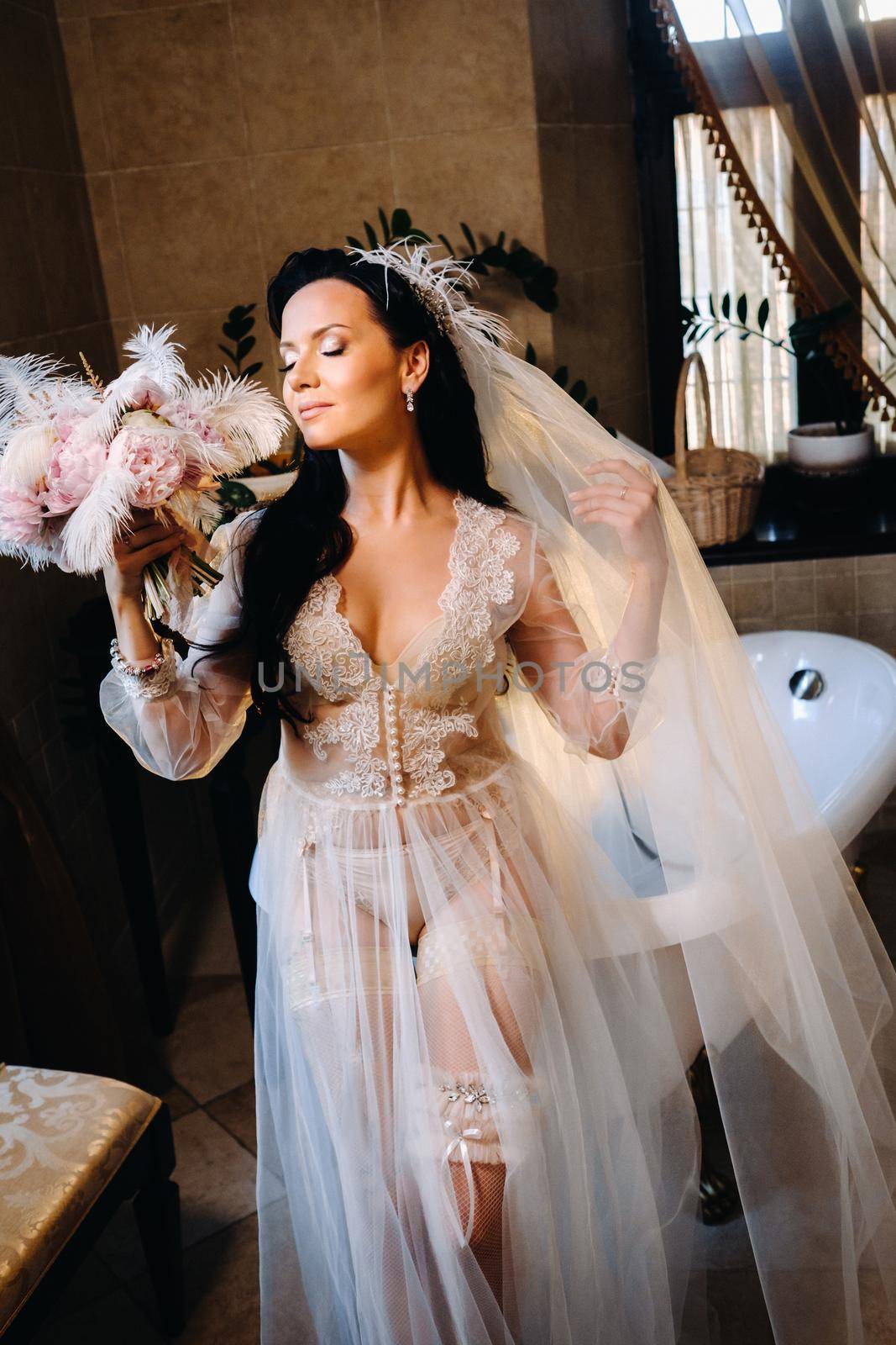 the bride, dressed in a boudoir transparent dress and underwear, sits near a vintage bath with a feather in her hands, The morning of the bride.