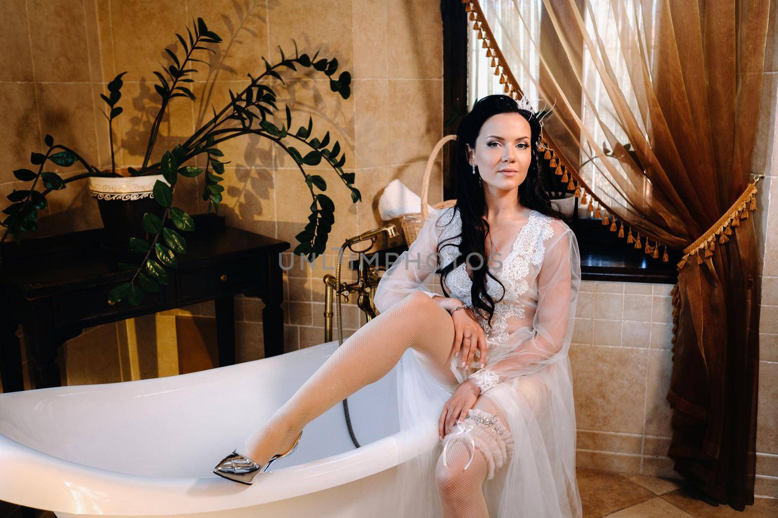 the bride, dressed in a boudoir transparent dress and underwear, is sitting on a vintage bathtub. Morning of the bride.