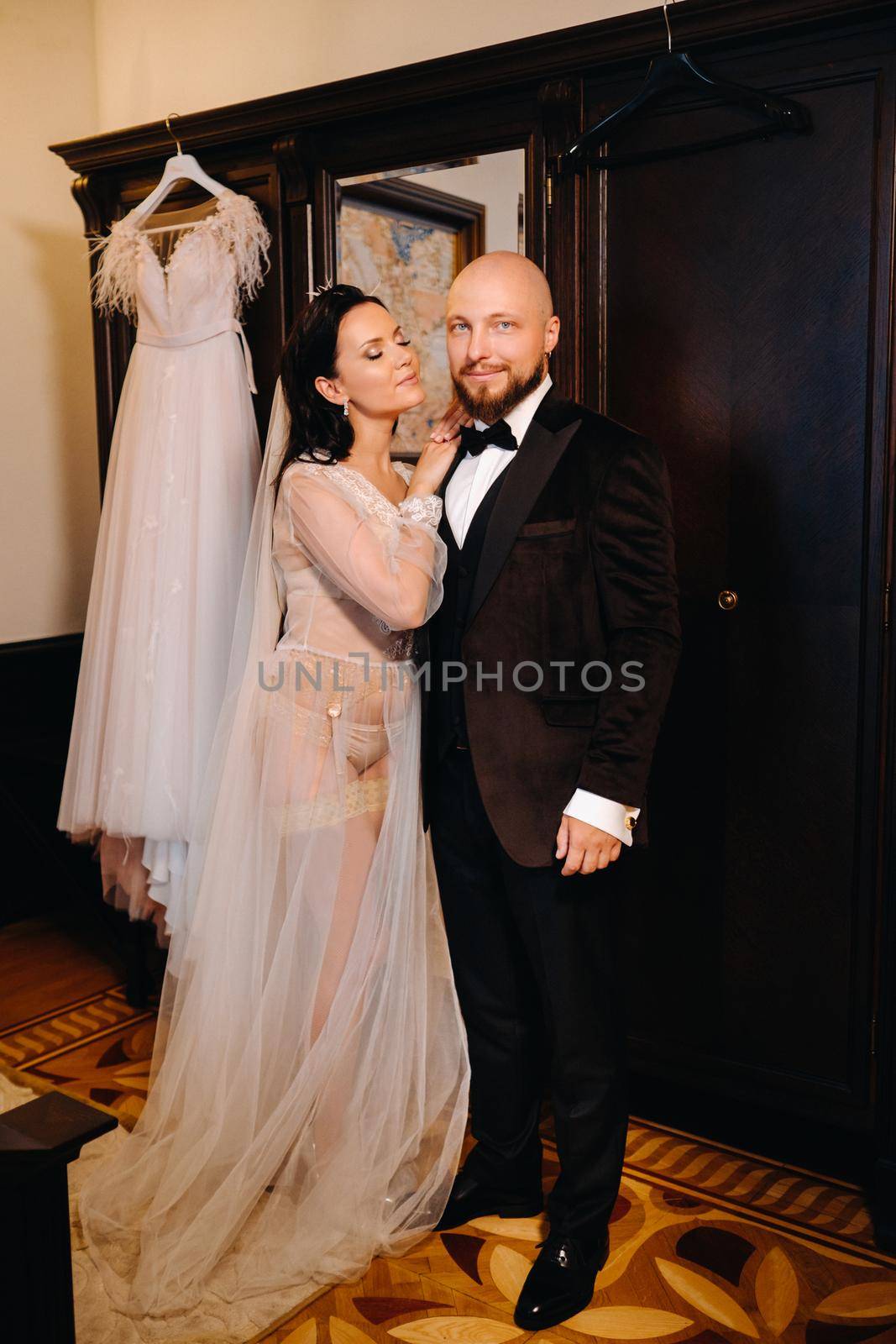 The bride in boudoir underwear dresses the groom in the interior of the hotel by Lobachad
