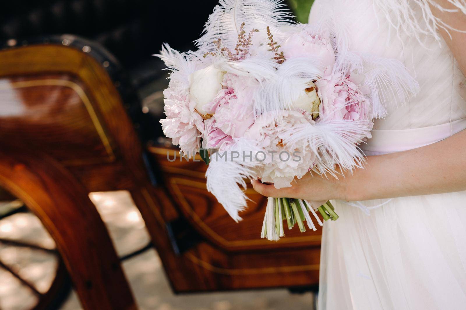 Close-up of a wedding bouquet of roses decorated with white feathers in the hands of the bride.