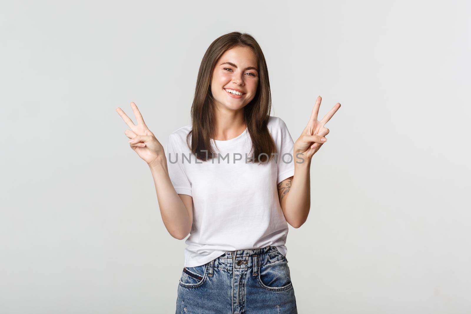Cheerful attractive young woman smiling, showing peace gestures.