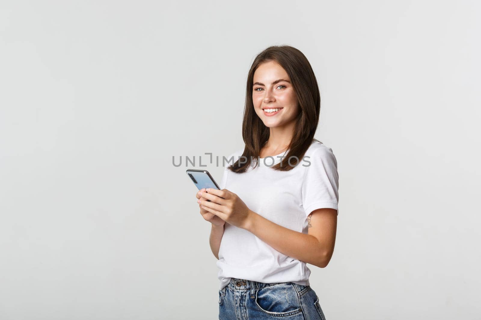 Attractive young brunette woman using mobile phone and smiling at camera by Benzoix