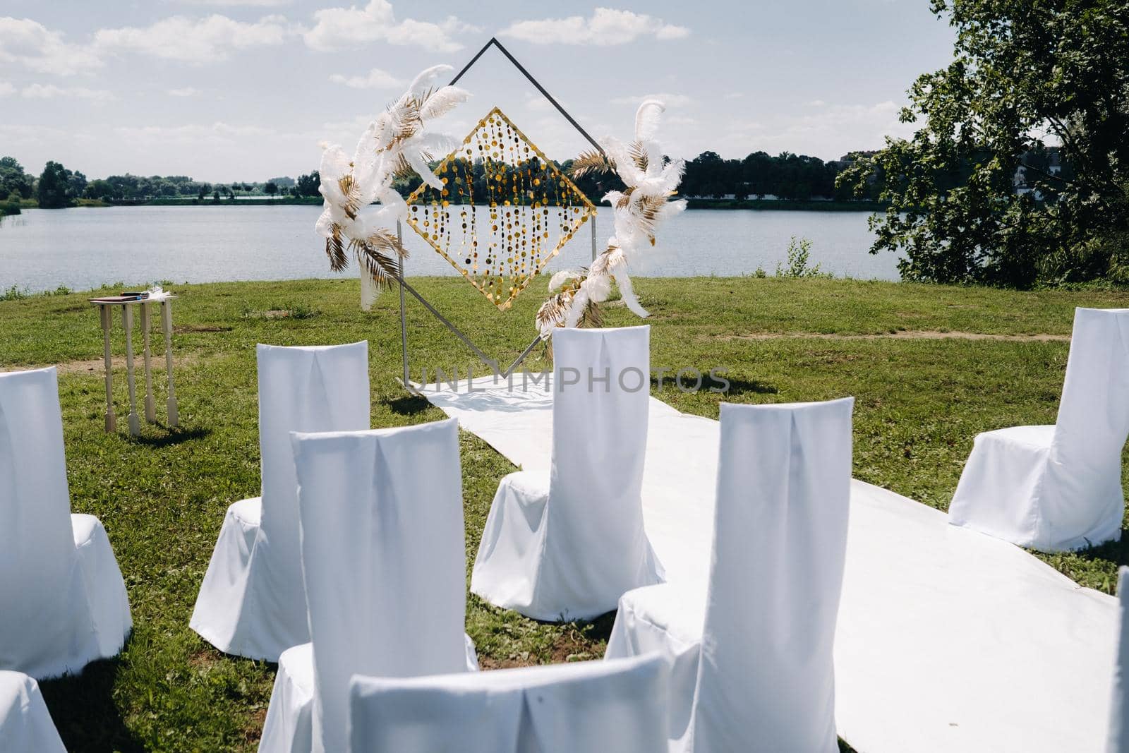 Decorated wedding arch in nature.Wedding ceremony with an arch decorated with retro-style feathers on a lake background.