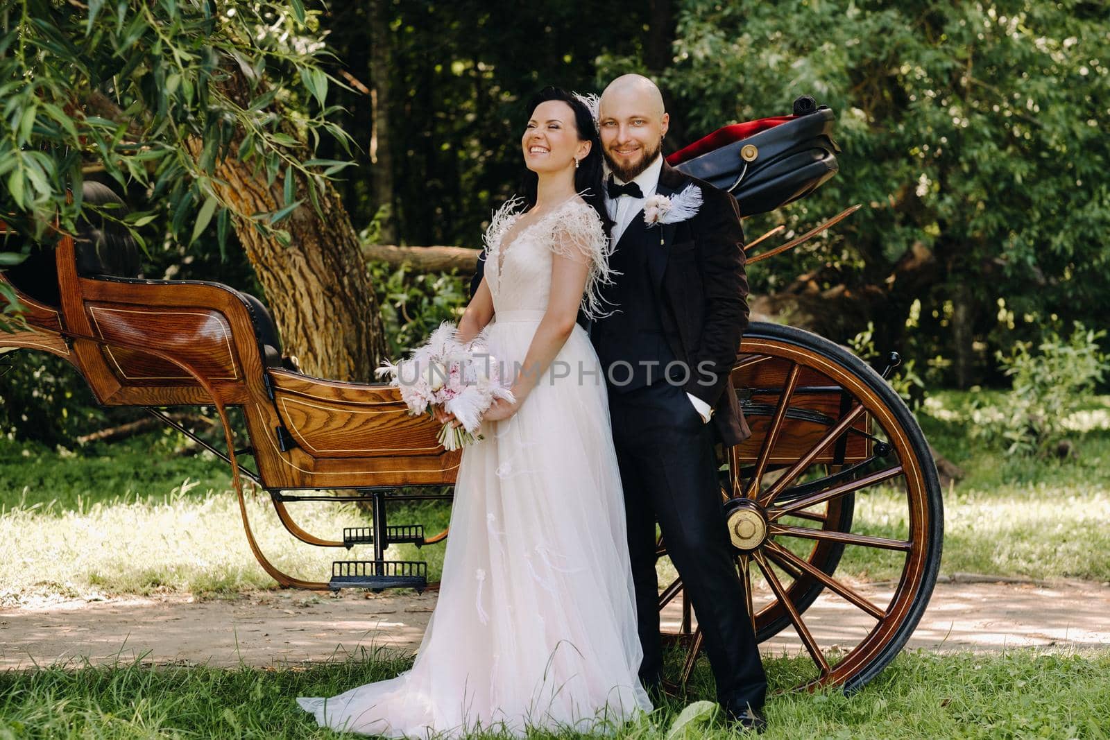 A couple of the bride and groom are standing near the carriage in nature in retro style.