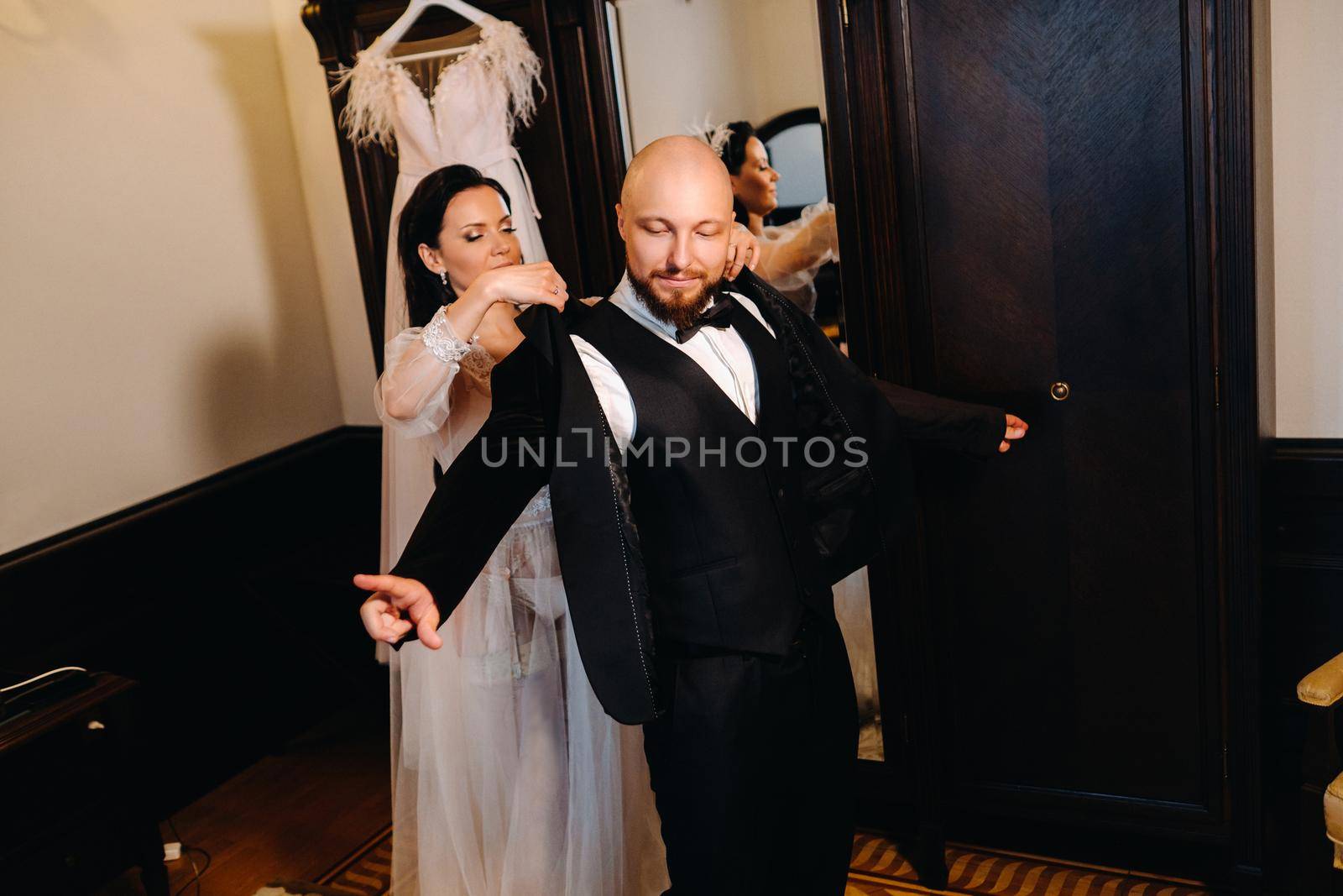 The bride in boudoir underwear dresses the groom in the interior of the hotel.