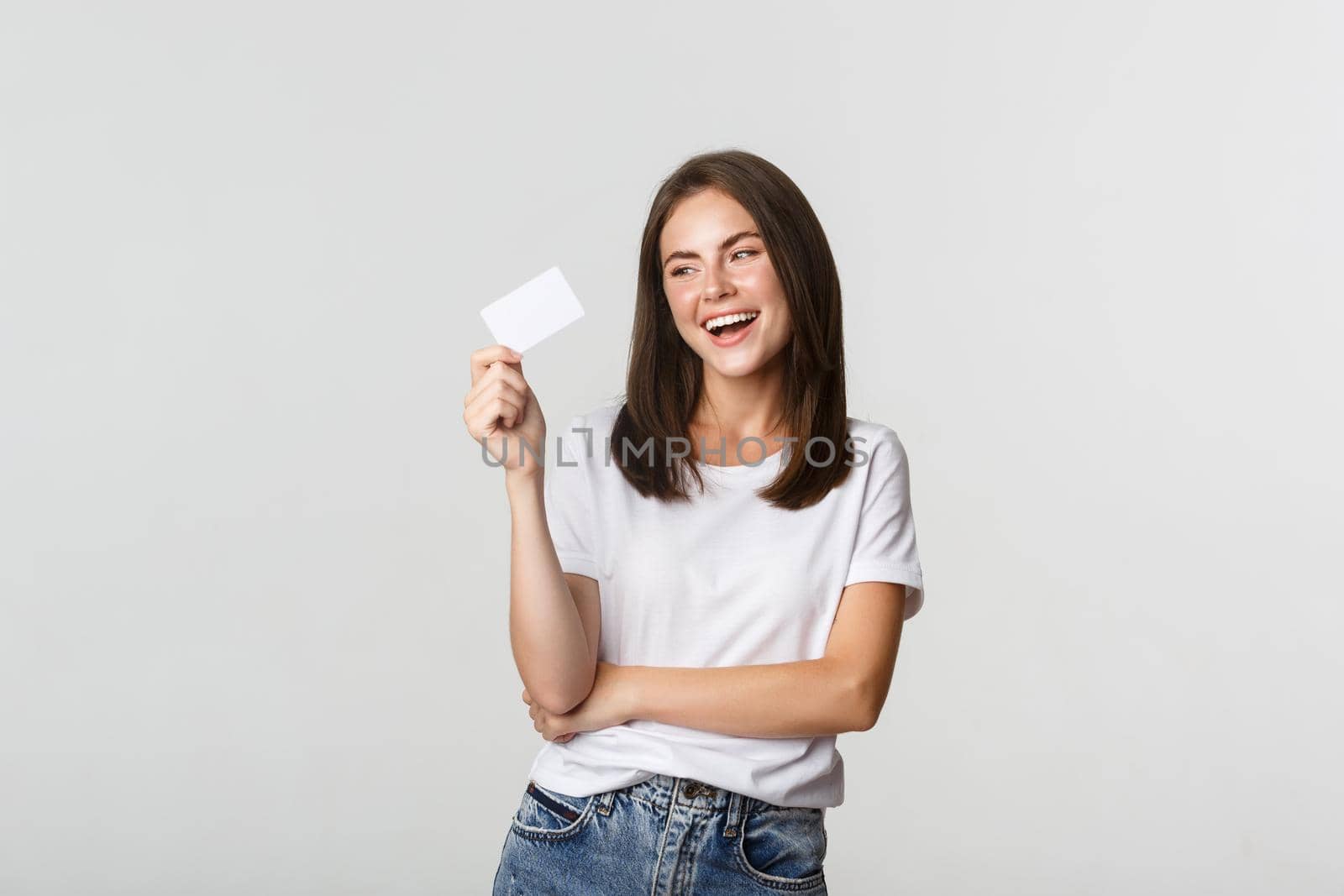 Attractive happy brunette girl laughing and holding credit card, white background.