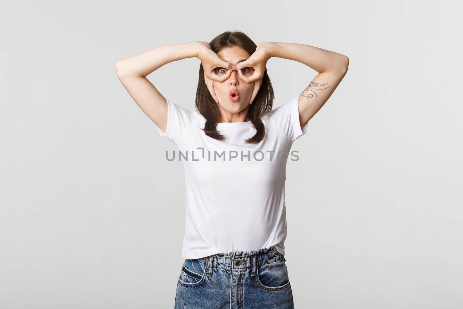 Amused cute brunette girl looking surprised and making hand glasses gesture.