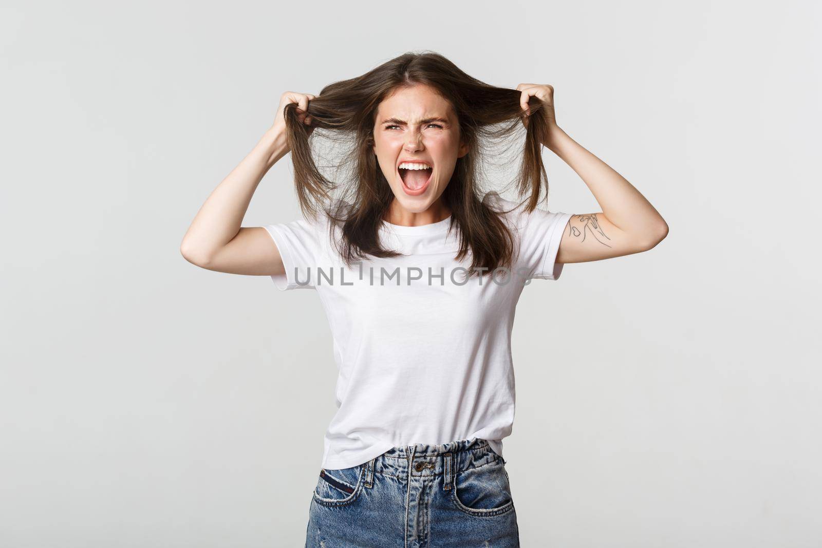 Outraged mad young woman ripping hair on head and yelling angry.