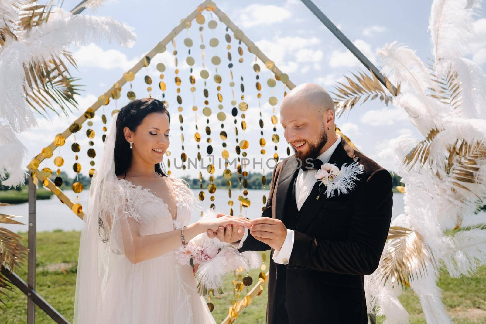 happy wedding couple near the arch wearing rings during the wedding ceremony.