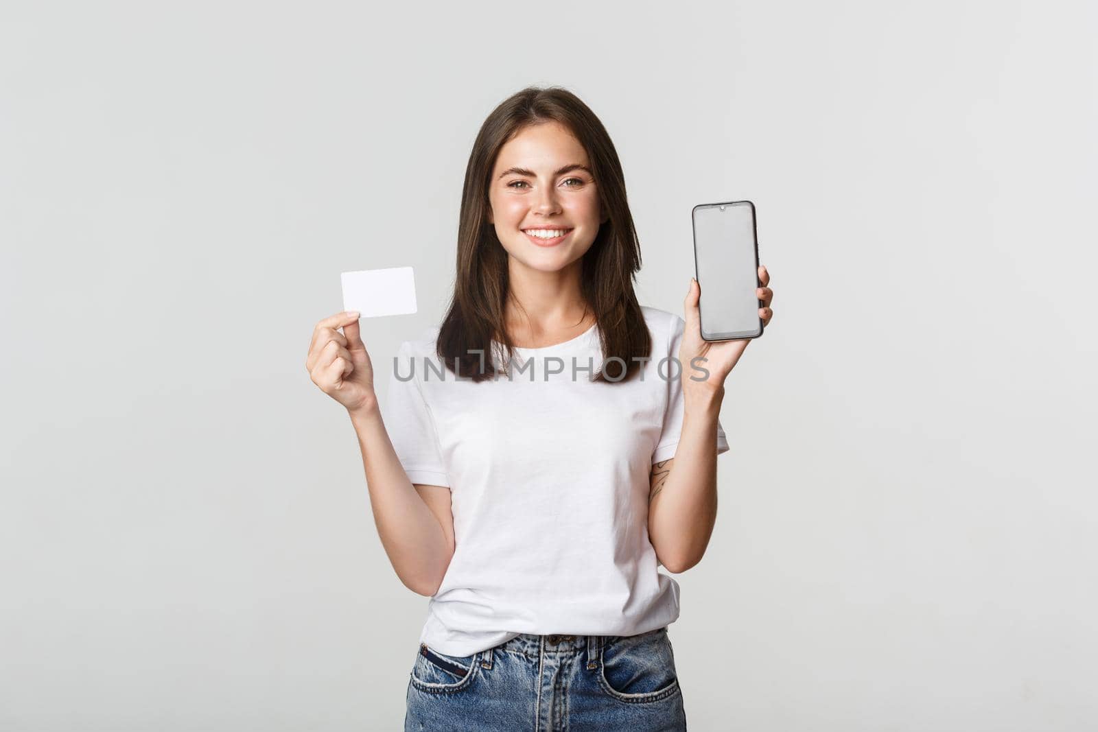 Attractive smiling girl looking satisfied and showing credit card, mobile phone screen.