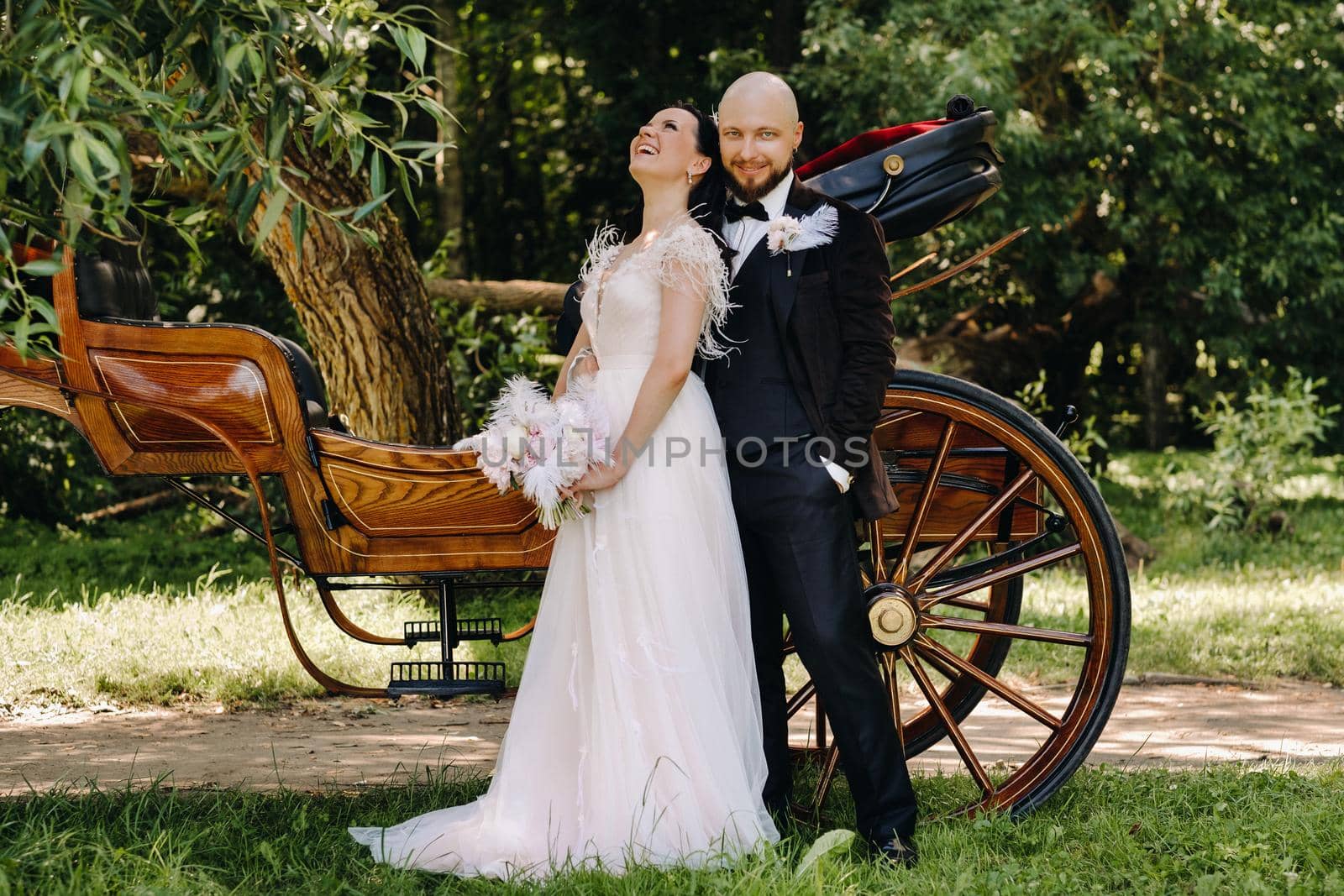 A couple of the bride and groom are standing near the carriage in nature in retro style.