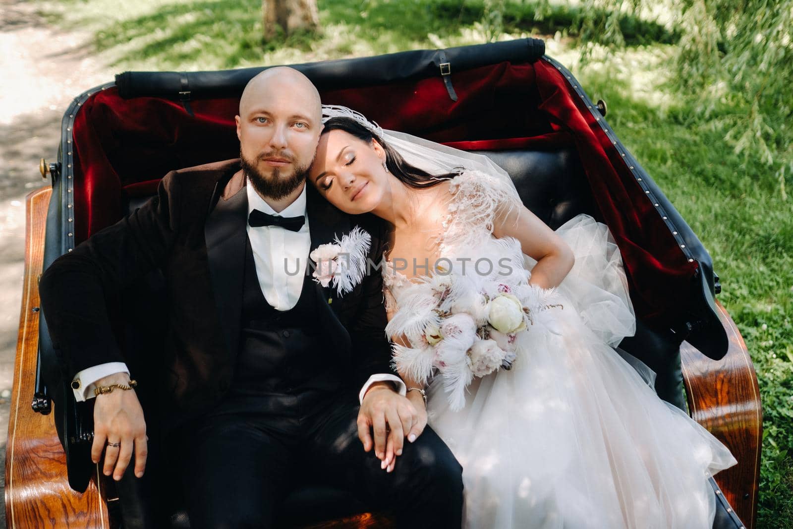 The bride and groom with a bouquet are sitting in a carriage in nature in retro style.