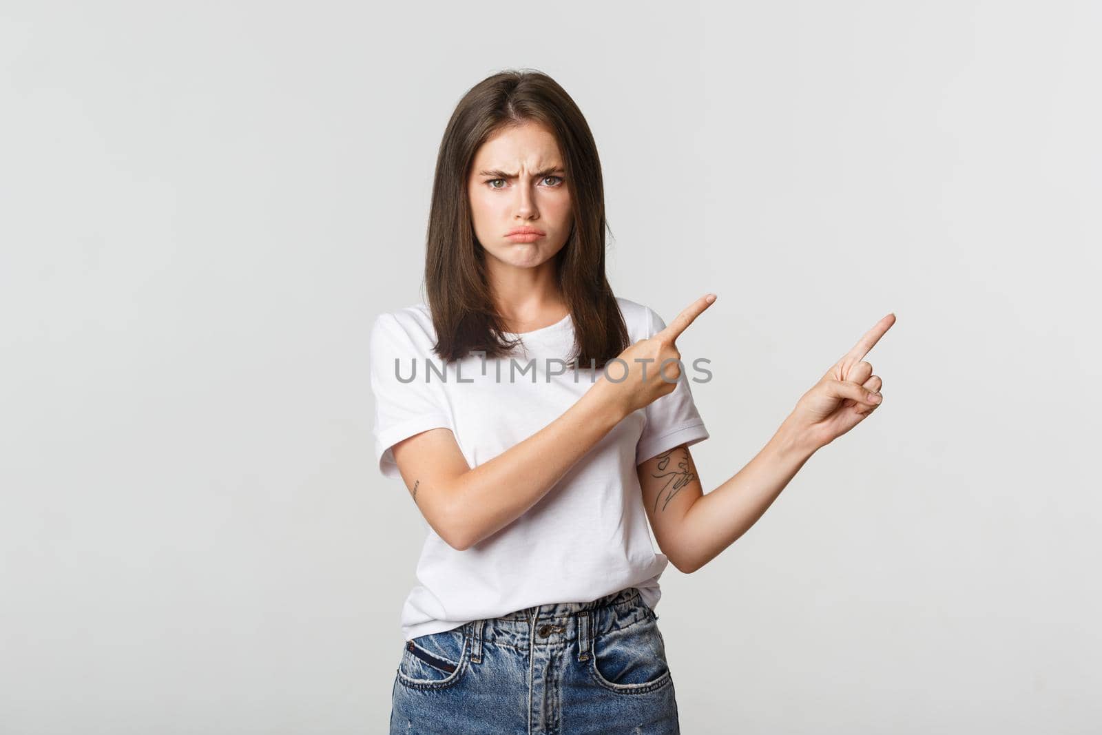 Disappointed sulking girl pointing fingers upper right corner, frowning and complaining.