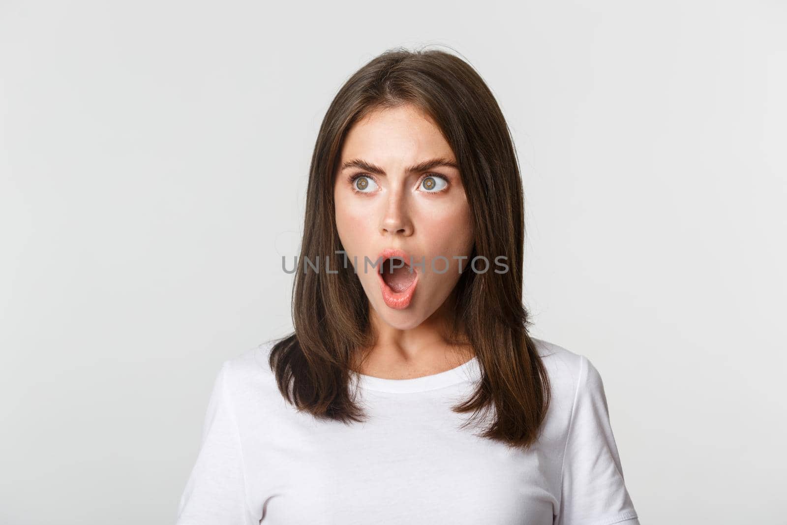 Portrait of impressed pretty girl looking left, drop jaw and gasping astonished, white background.