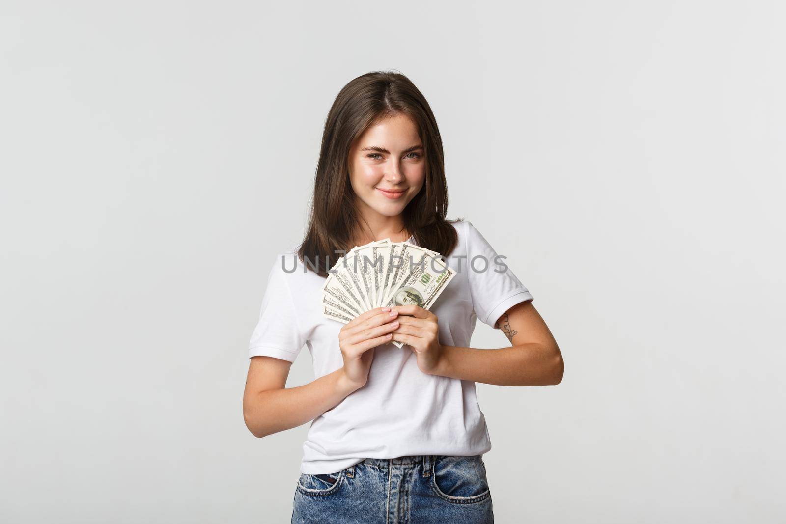 Greedy smiling girl looking cunning and holding money, standing white background.
