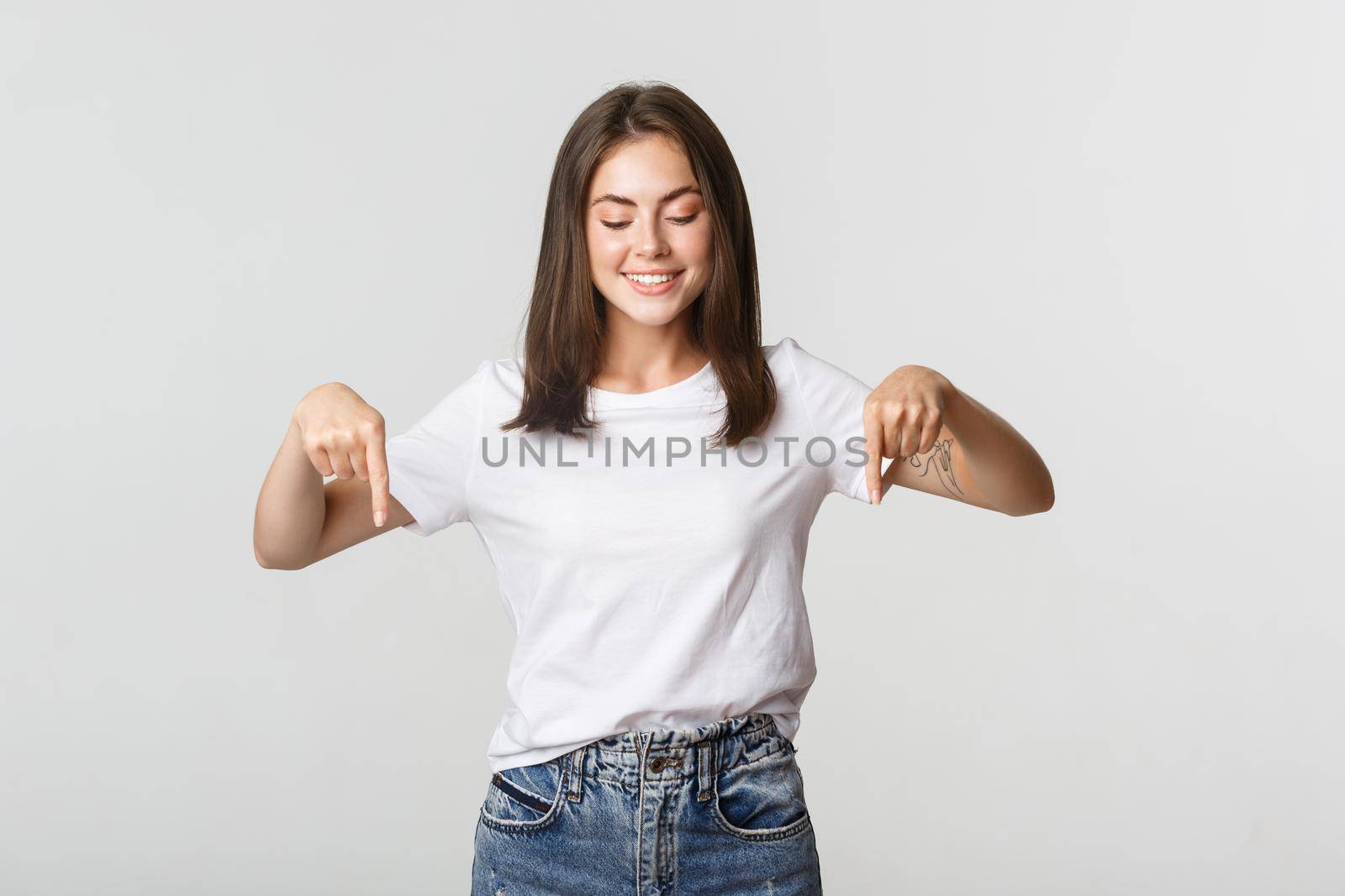 Excited happy brunette girl, looking and pointing down with satisfied smile.