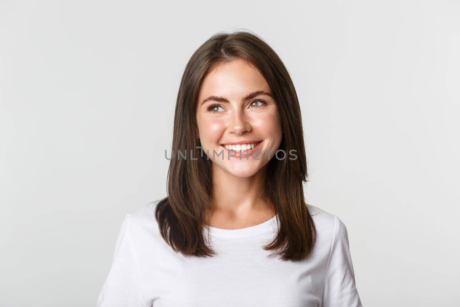 Portrait of attractive thoughtful girl smiling and looking left, white background.