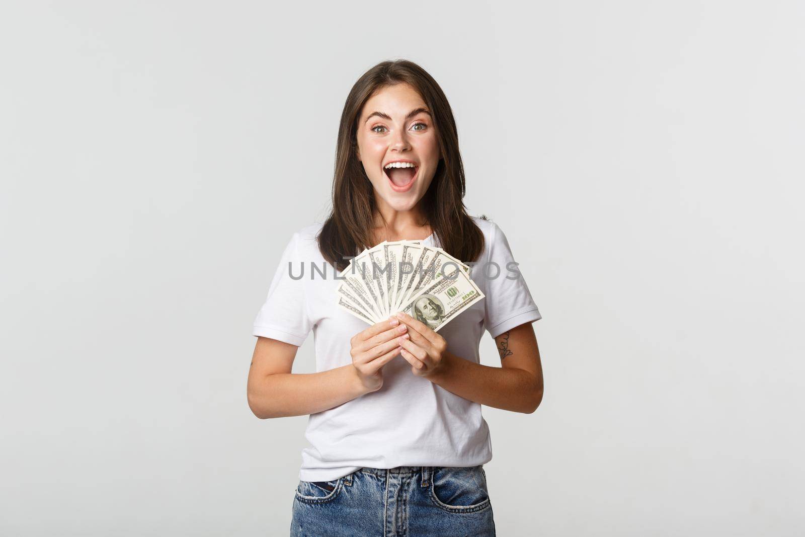 Happy attractive brunette girl holding money and smiling excited, white background.