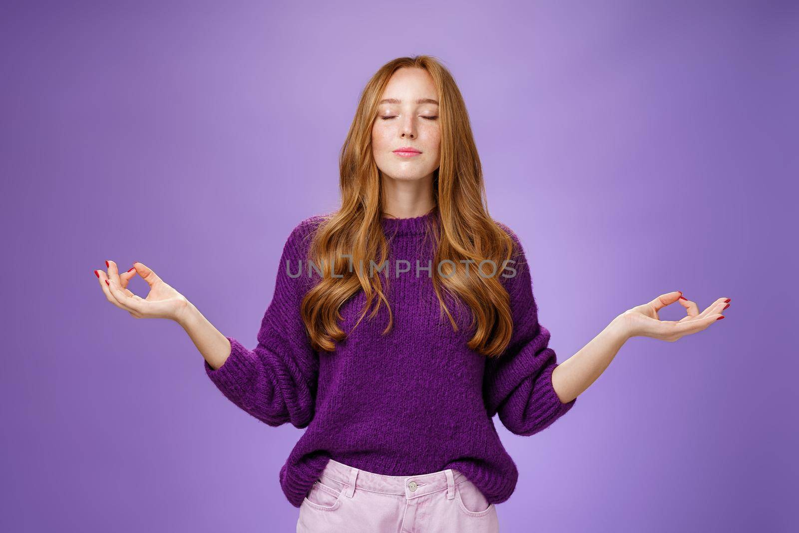 Sound mind in body. Peaceful and happy attractive female with red hair and freckles close eyes and smile from calm and relieved feelings as meditating in lotus pose with mudra gesture, doing yoga.