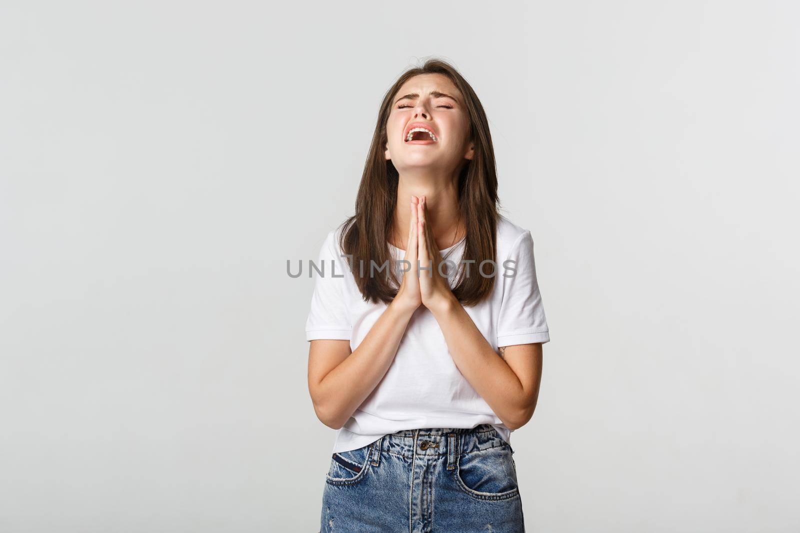 Miserable brunette girl holding hands in pray and pleading, begging for help.