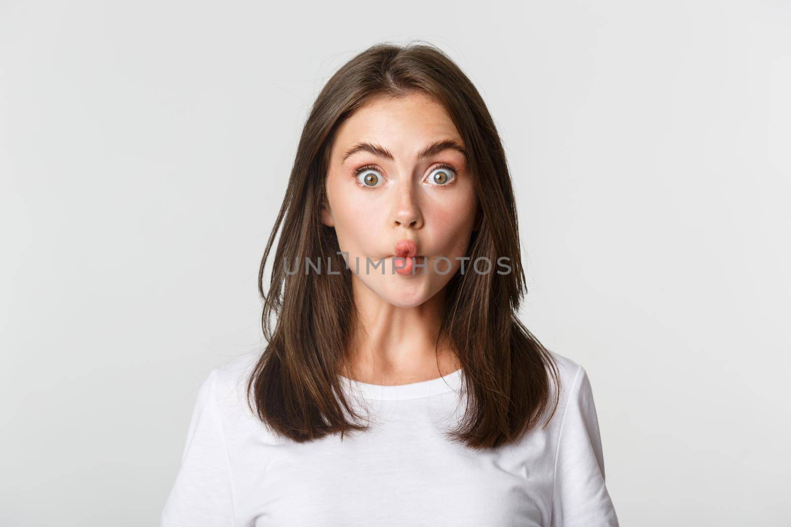 Close-up of funny and cute brunette girl suckink lips, making fish grimace, white background.