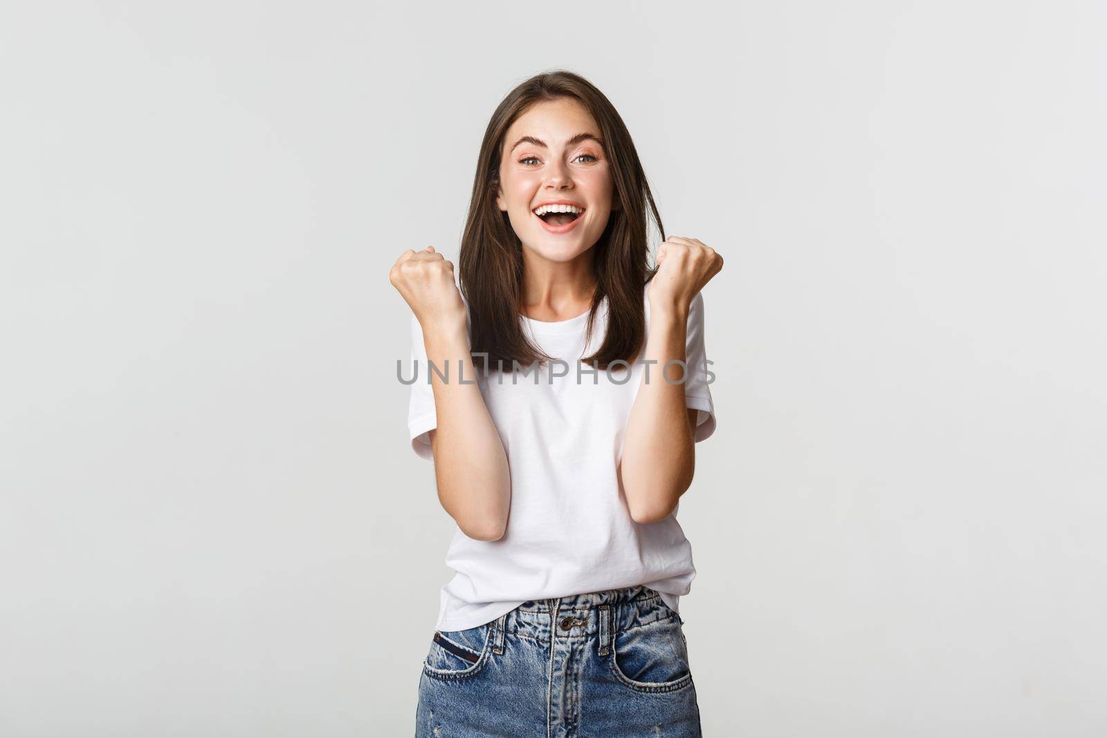 Cheerful attractive brunette girl fist pump and smiling with rejoice, winning.