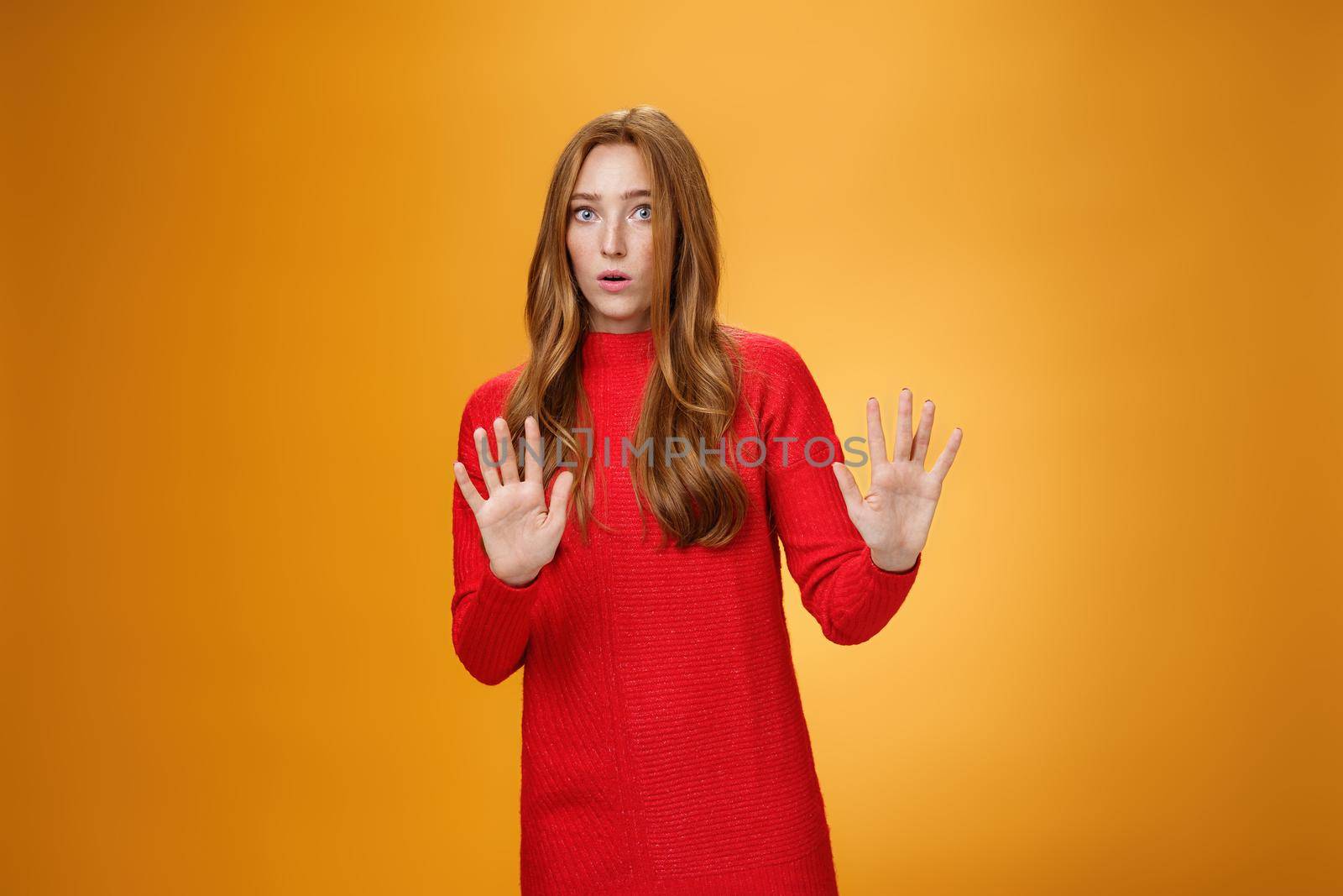 Intense panicking and freaked out girl with red hair asking slow down, raising hands near chest in stop and not gesture open mouth surpised and shocked, dismaying strange offer over orange background.