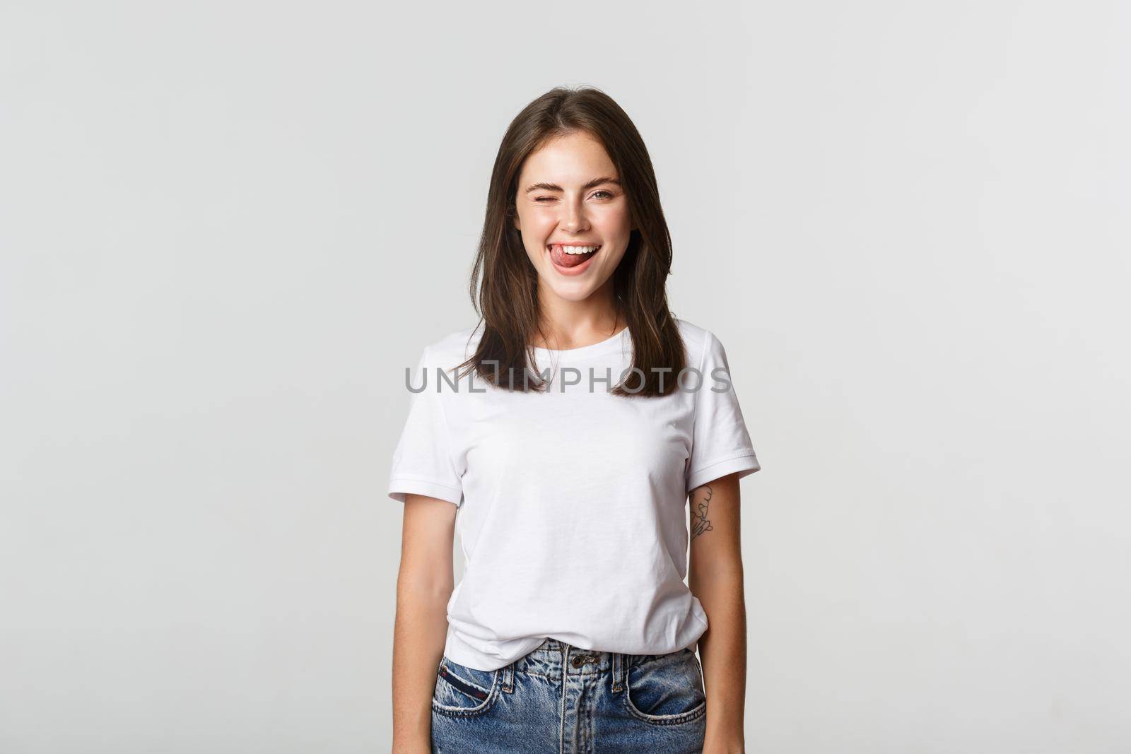 Sassy beautiful young woman winking and showing tongue flirty, white background.